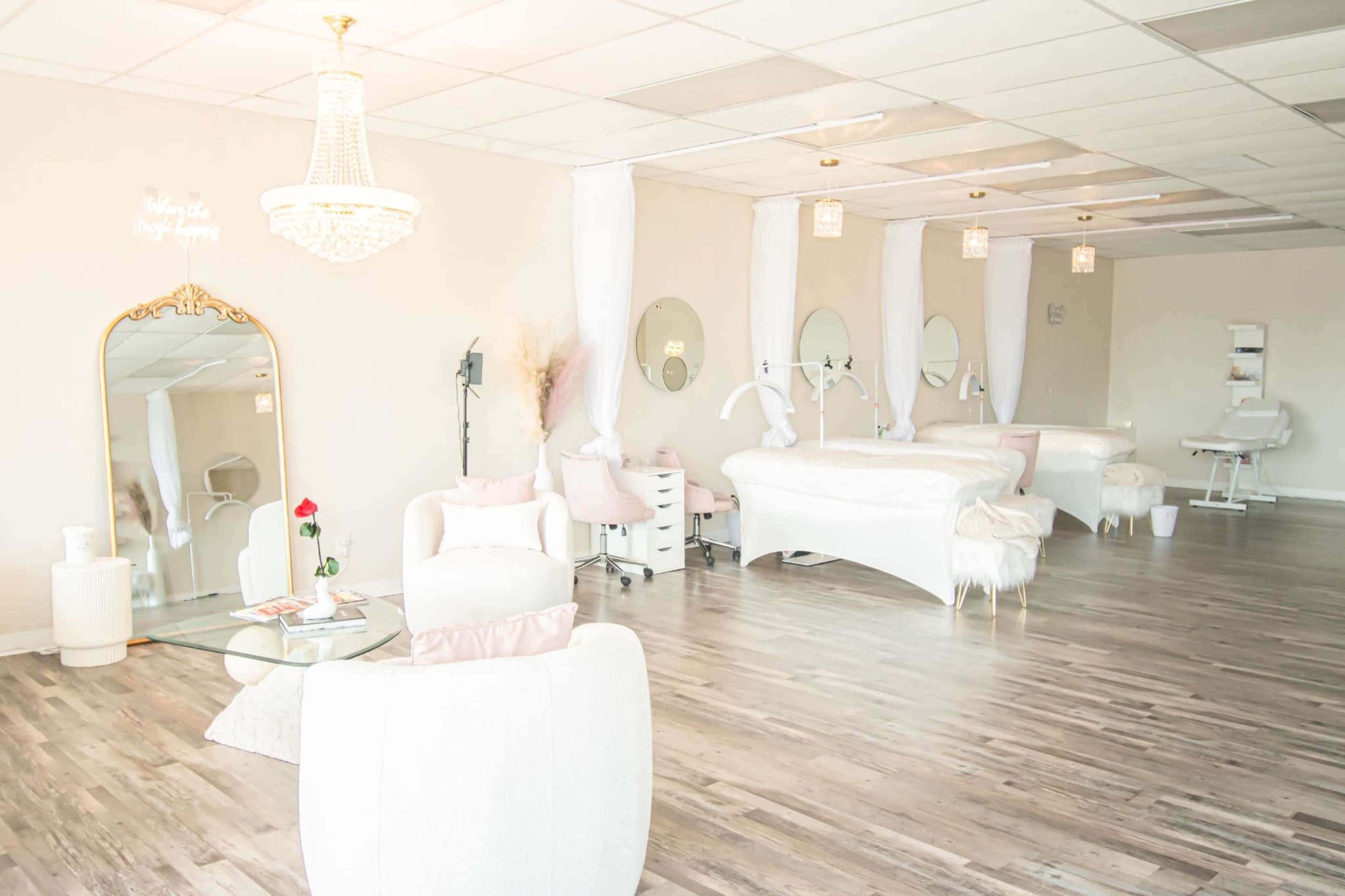 The image shows a bright and spacious salon interior with elegant furniture, including a treatment bed, mirrored surfaces, and decorative lighting.