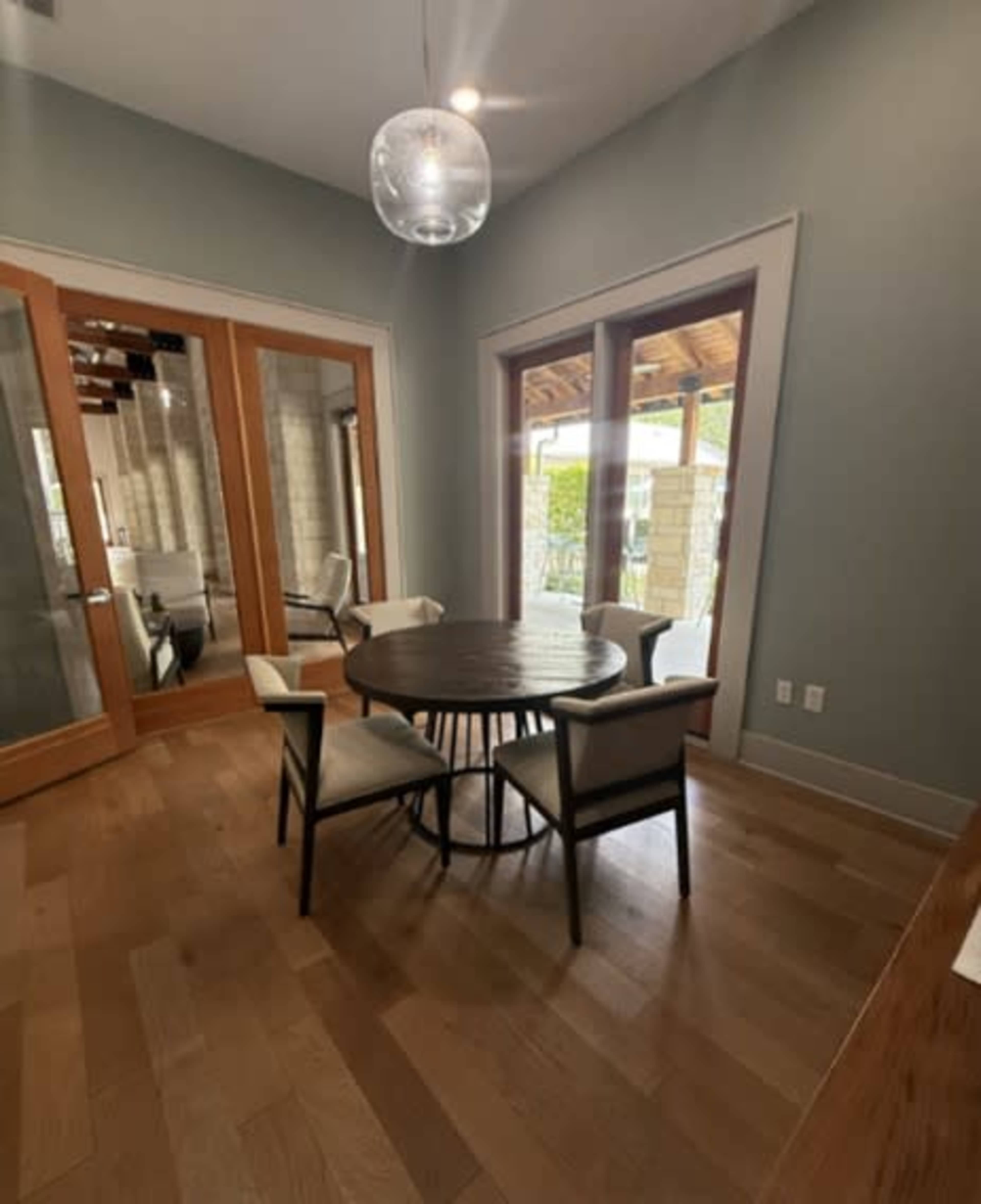 A dining area features a round wooden table surrounded by four chairs, with large glass doors leading to an outdoor space.