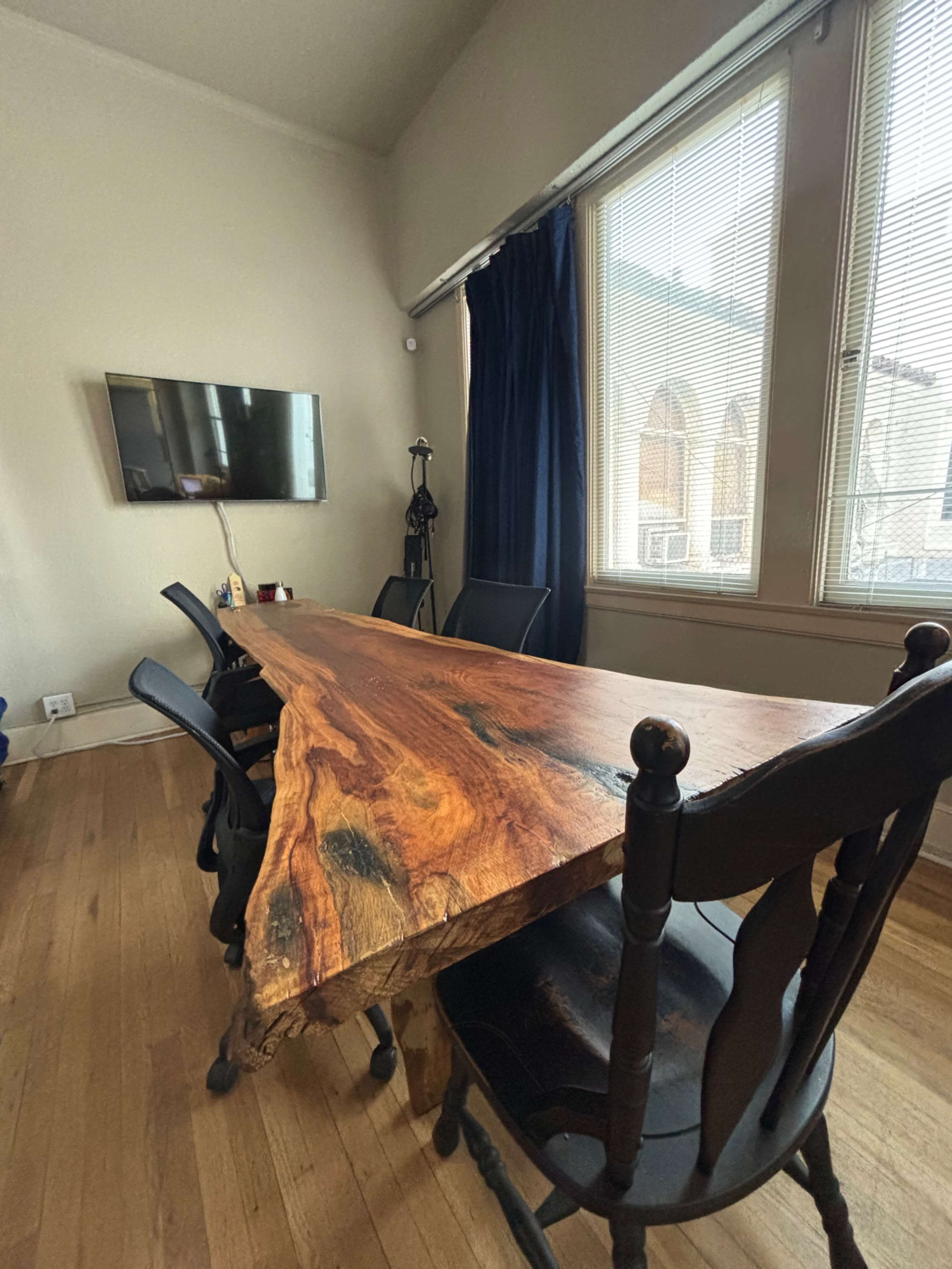 A wooden conference table with a natural edge is surrounded by black chairs in a well-lit room with large windows.