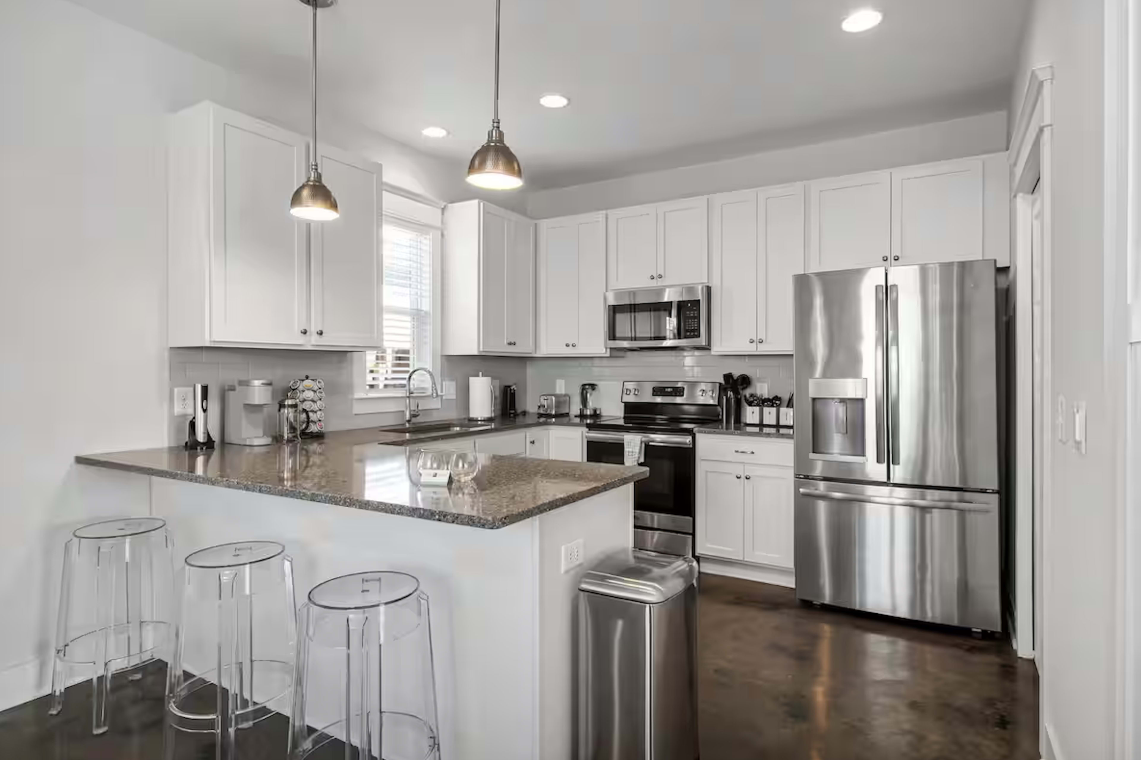 The image displays a modern kitchen featuring white cabinetry, stainless steel appliances, and a bar area with clear stools.