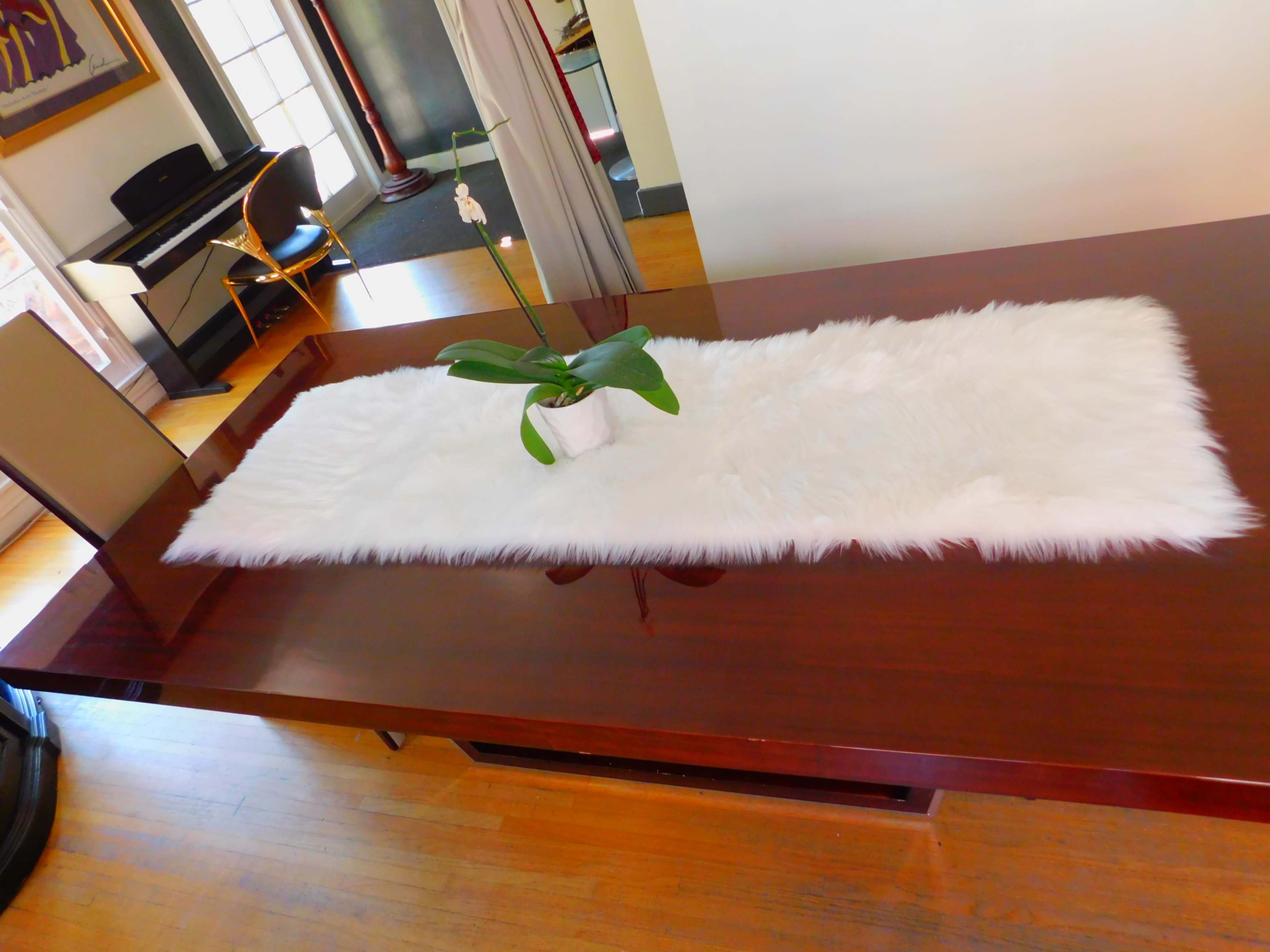 A long, white fur runner is placed on a polished wooden table with a small potted orchid in the center.