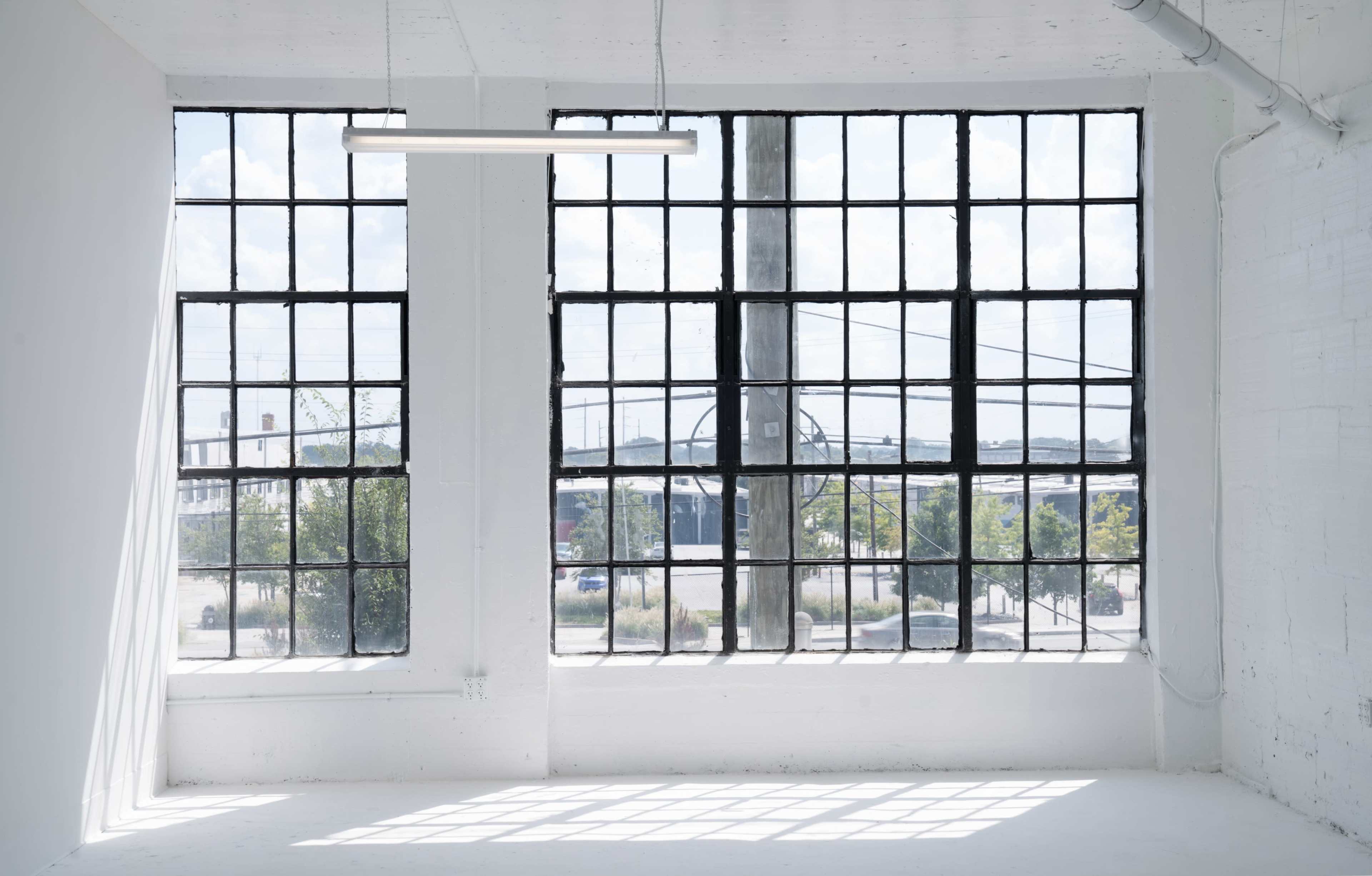 A bright, empty room with large industrial windows allowing natural light to flood in.