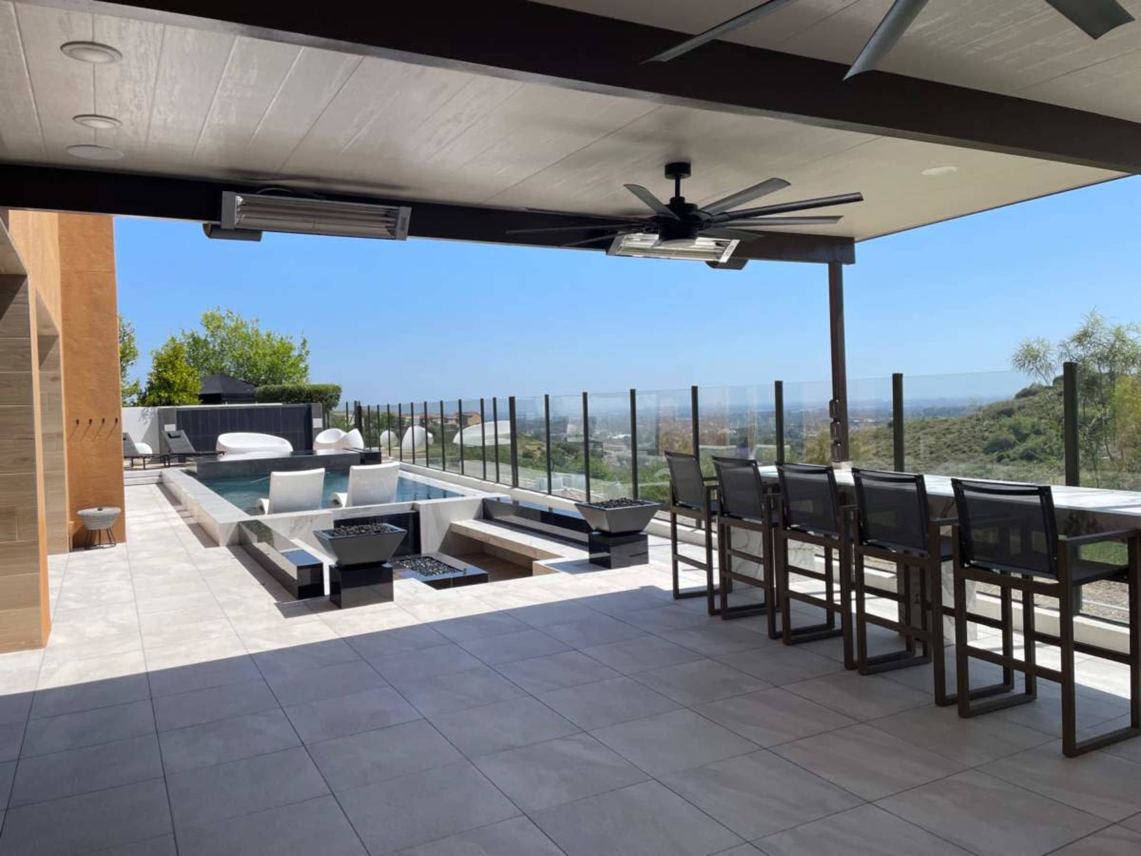 A modern outdoor patio features a pool, lounge chairs, and a dining area with a clear view of the surrounding landscape.