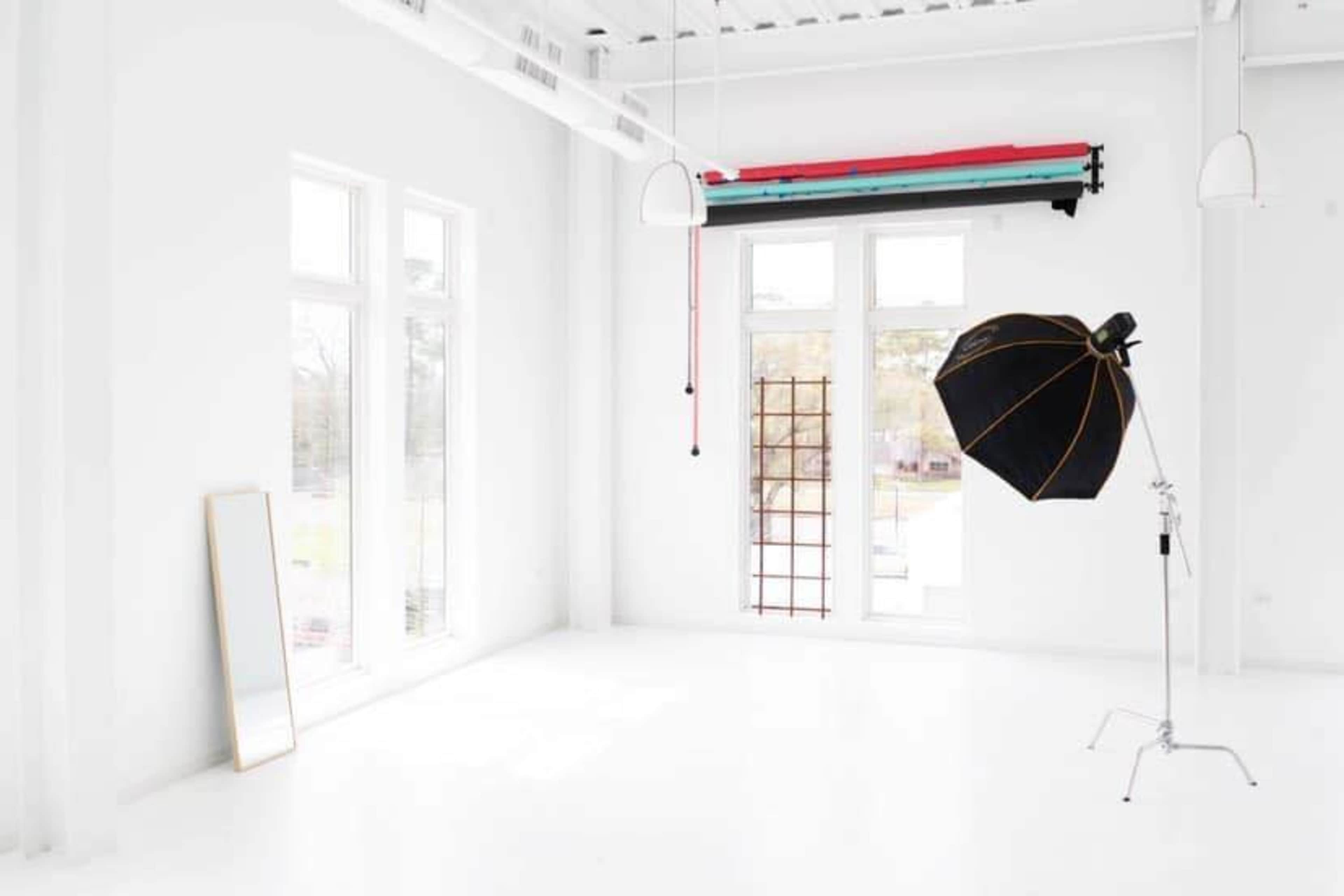 A bright, empty studio space with white walls, a large mirror, and a black photography umbrella on a silver stand.