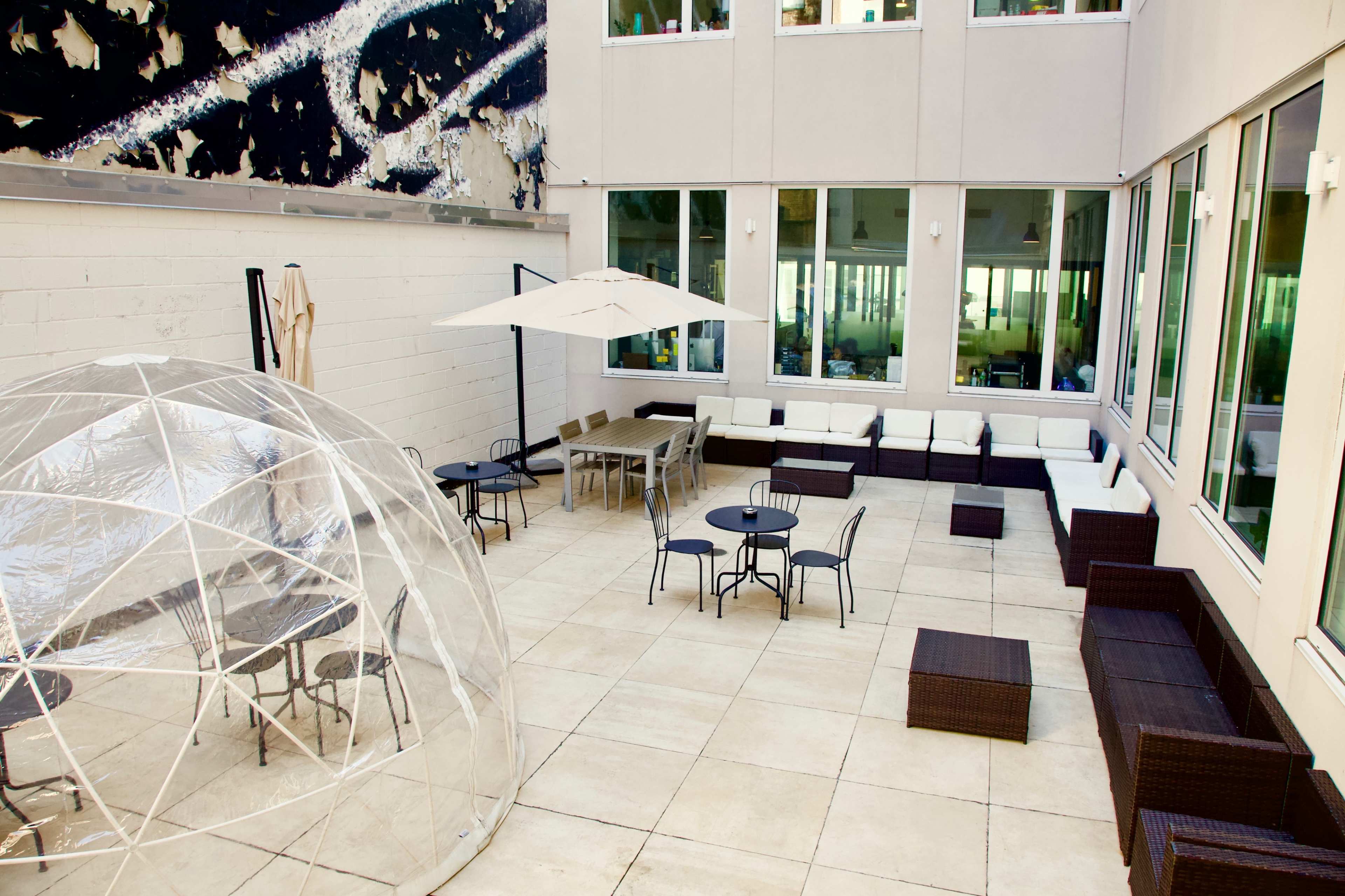 A modern outdoor lounge area featuring a clear dome structure, several seating arrangements, and a large umbrella.