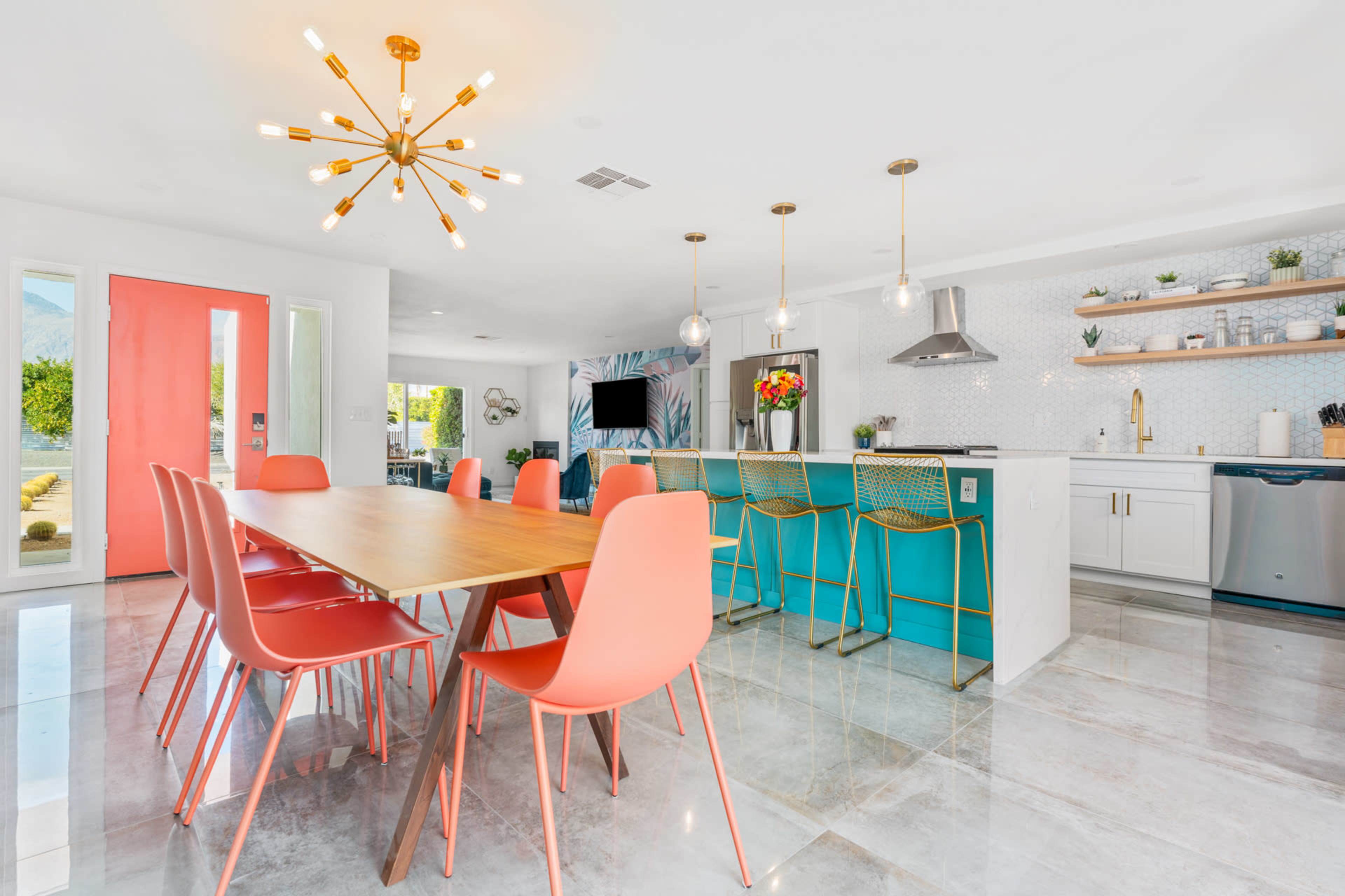 A modern kitchen and dining area with a wooden table surrounded by coral-colored chairs and a turquoise kitchen island.