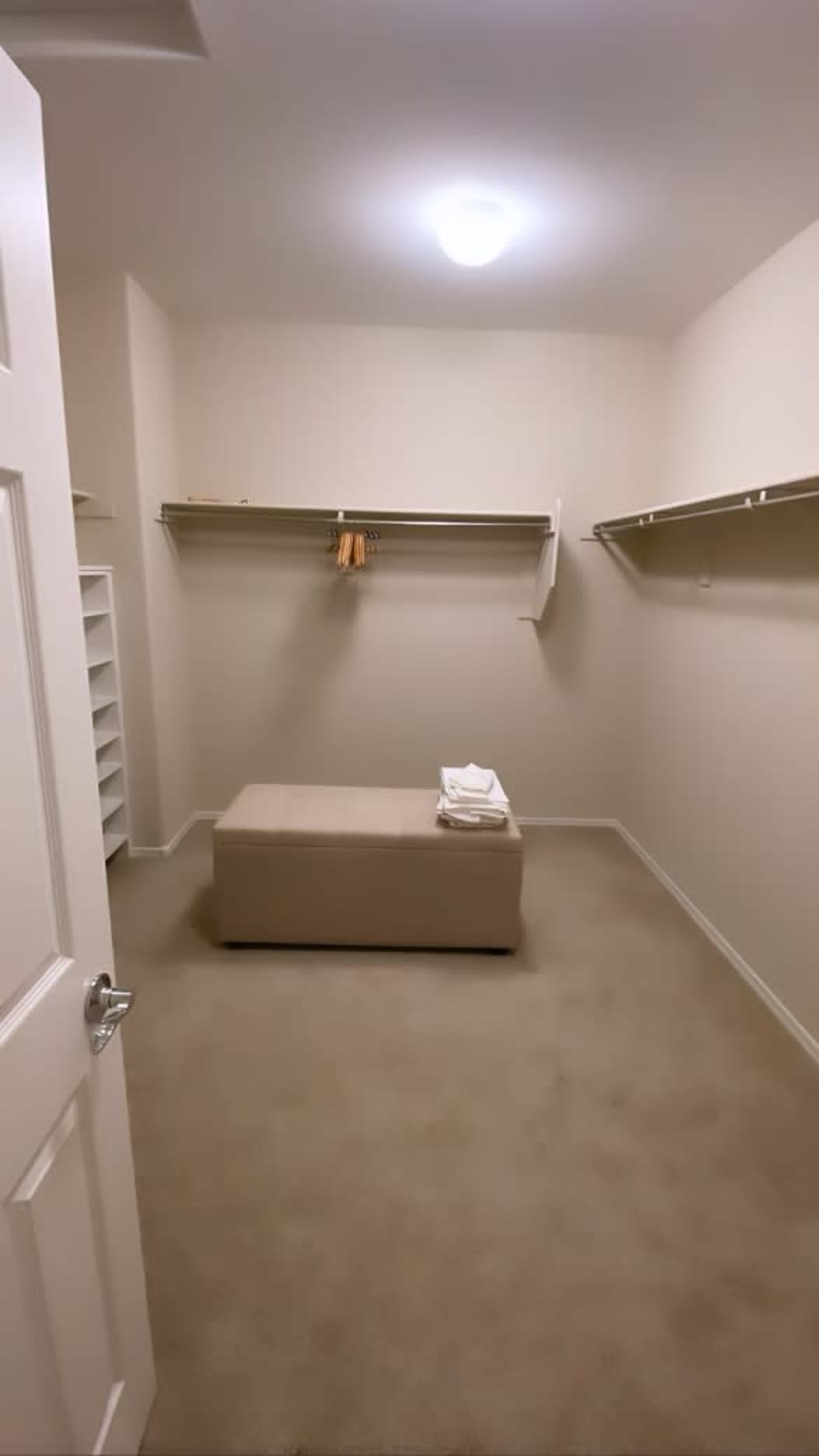 The image shows an empty walk-in closet with beige carpet, a central bench, and shelves lining the walls.