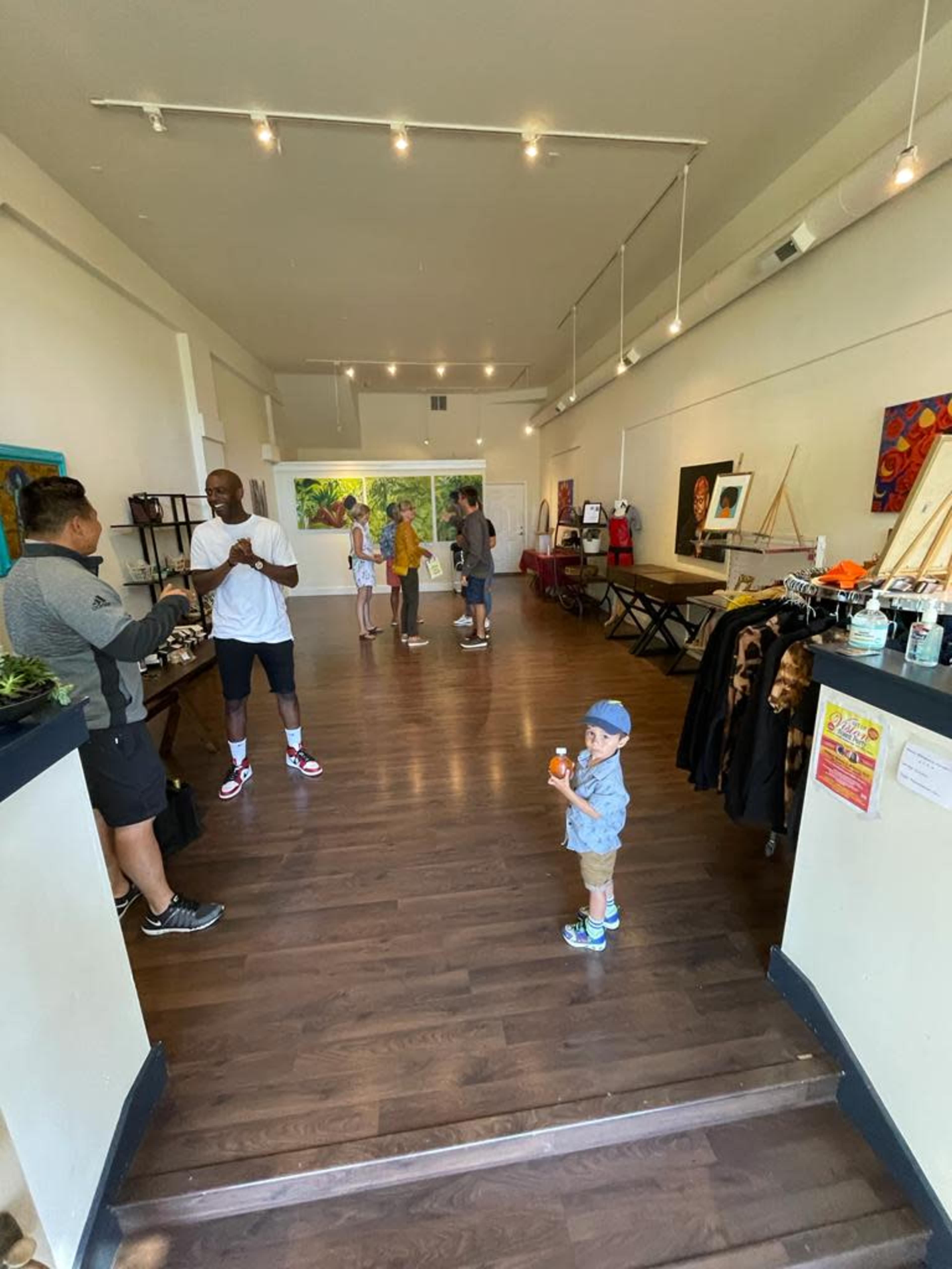 A spacious art gallery with several people browsing and engaging, while a young boy holds an ice cream cone near the entrance.