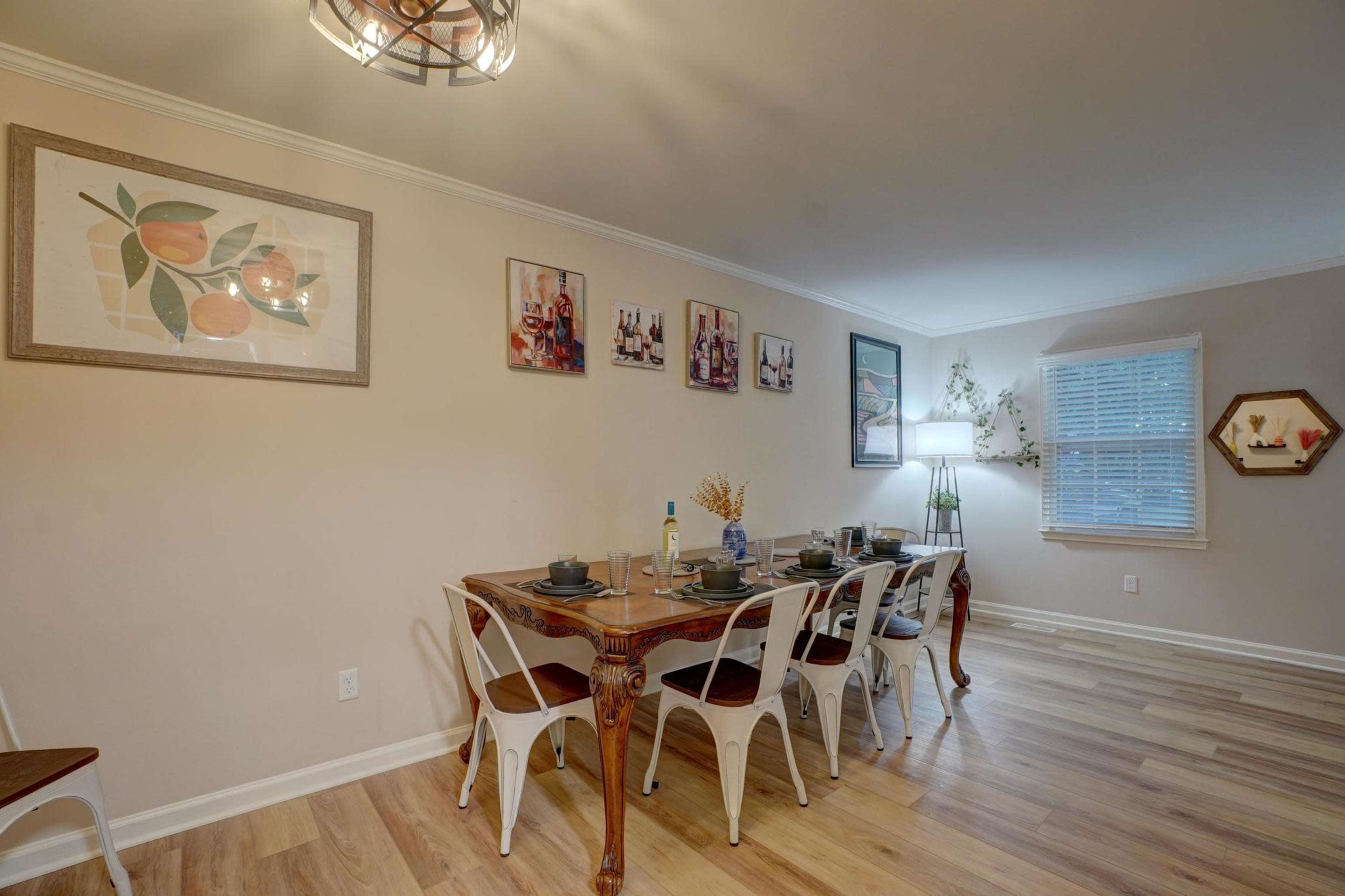 A dining area features a table set with plates and utensils, surrounded by white chairs, and adorned with framed artwork on the walls.