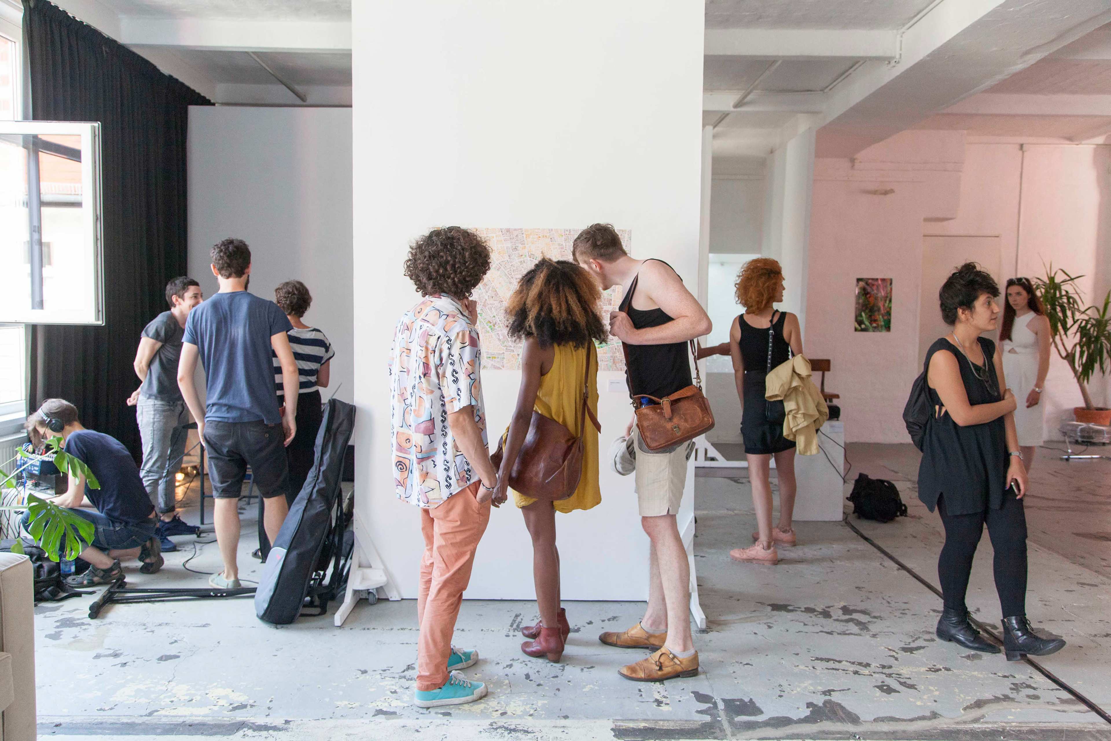 A group of people are viewing artwork in a spacious, brightly lit gallery with a mix of plants and minimalist decor.
