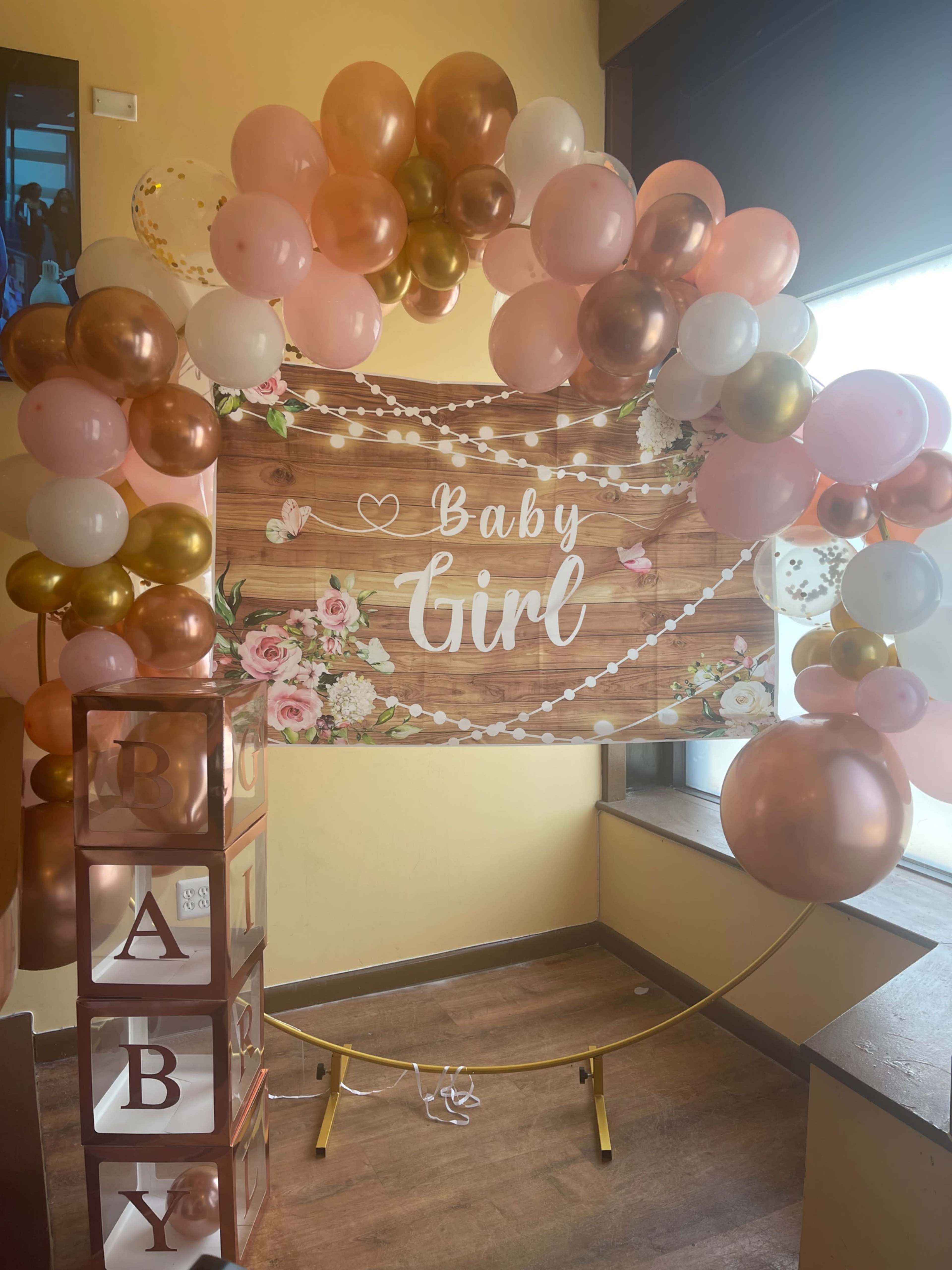 A decorative balloon arch with a sign that reads "Baby Girl," set up in a brightly lit indoor space.