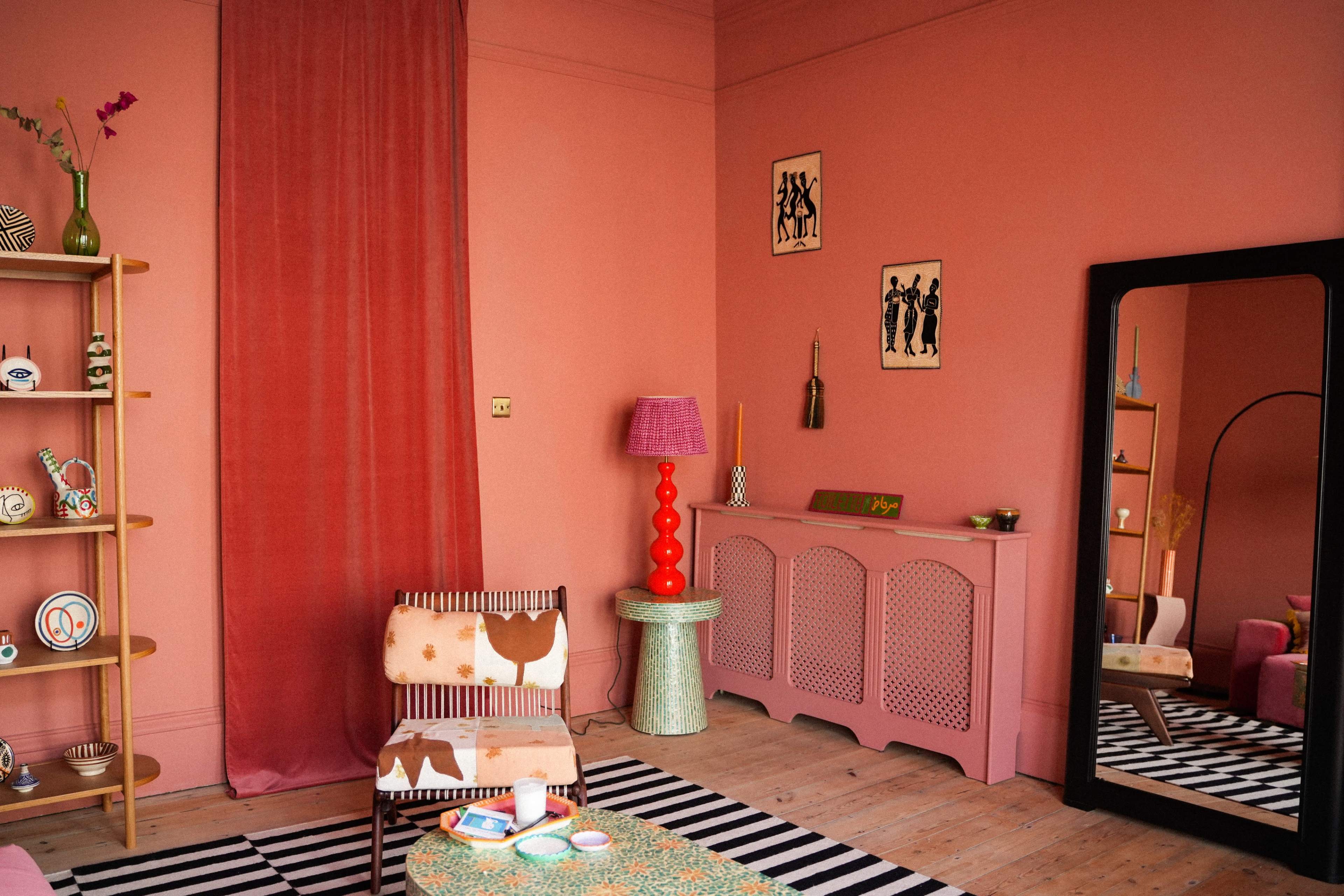 The room features pink walls, a striped rug, colorful decor items, and a large mirror reflecting the space.