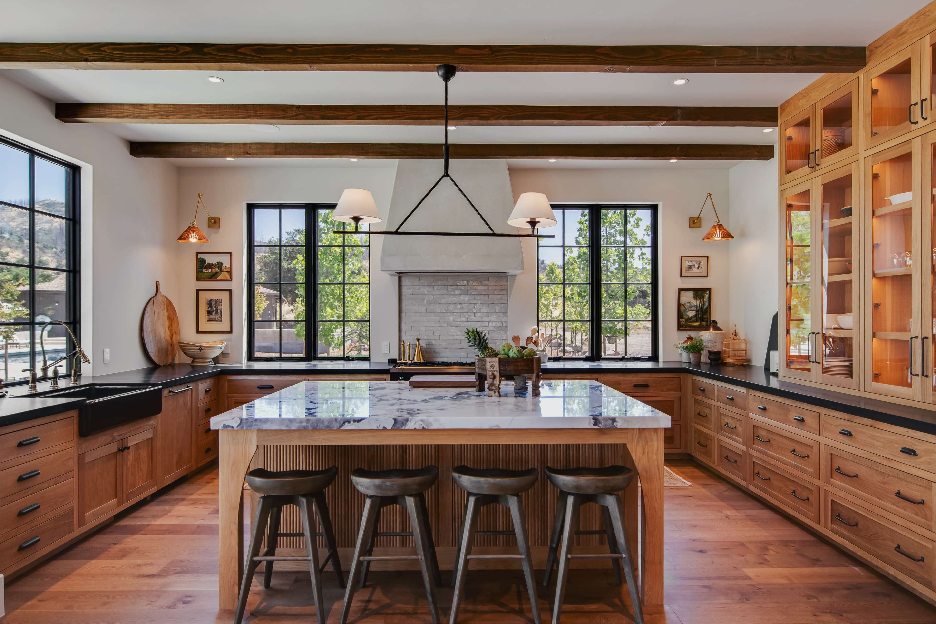 The kitchen features a large central island with a marble countertop, wooden cabinetry, and windows providing natural light.