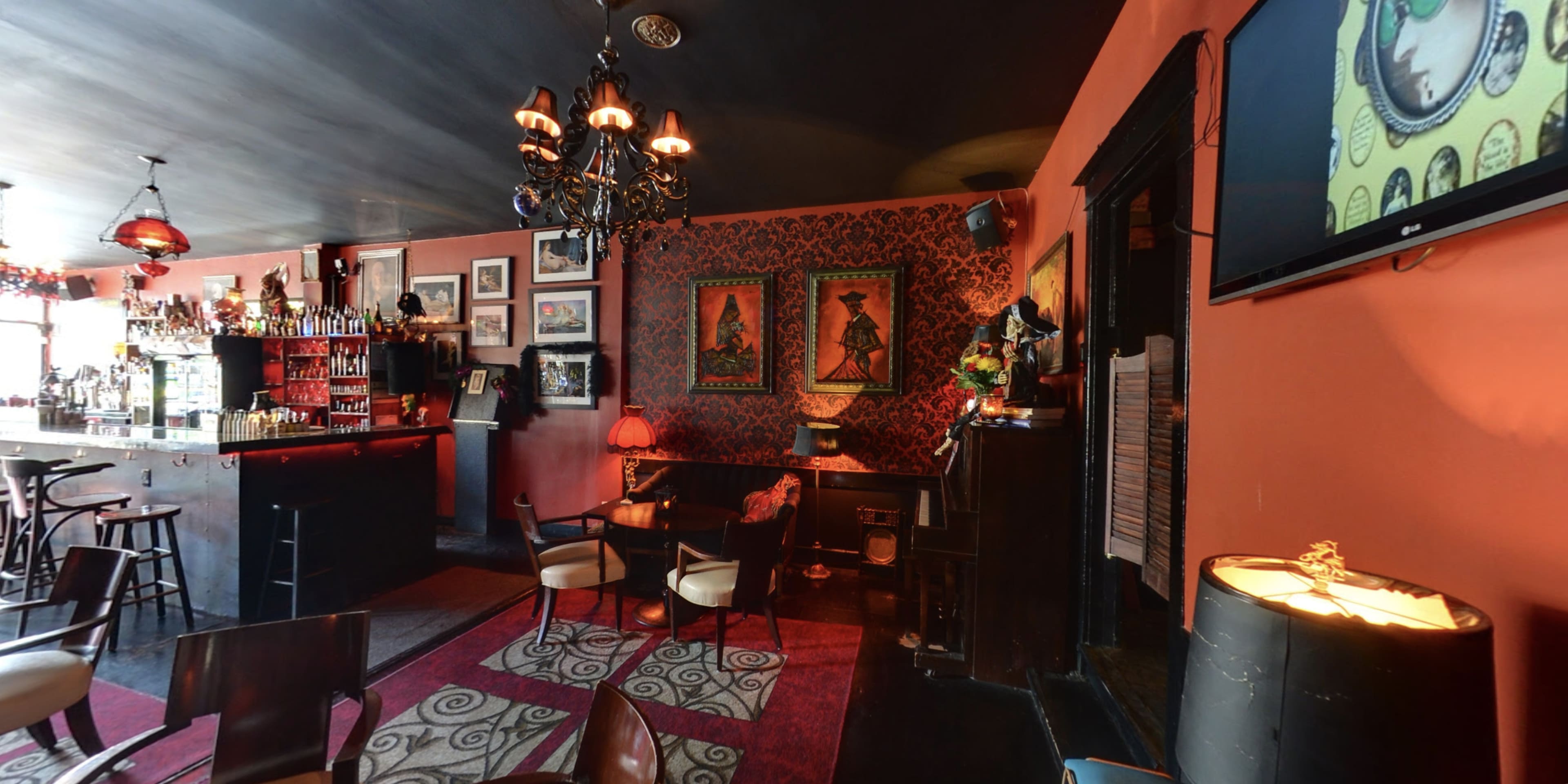 A dimly lit bar features a mix of elegant furnishings, colorful artwork on the walls, and a prominent bar counter stocked with drinks.