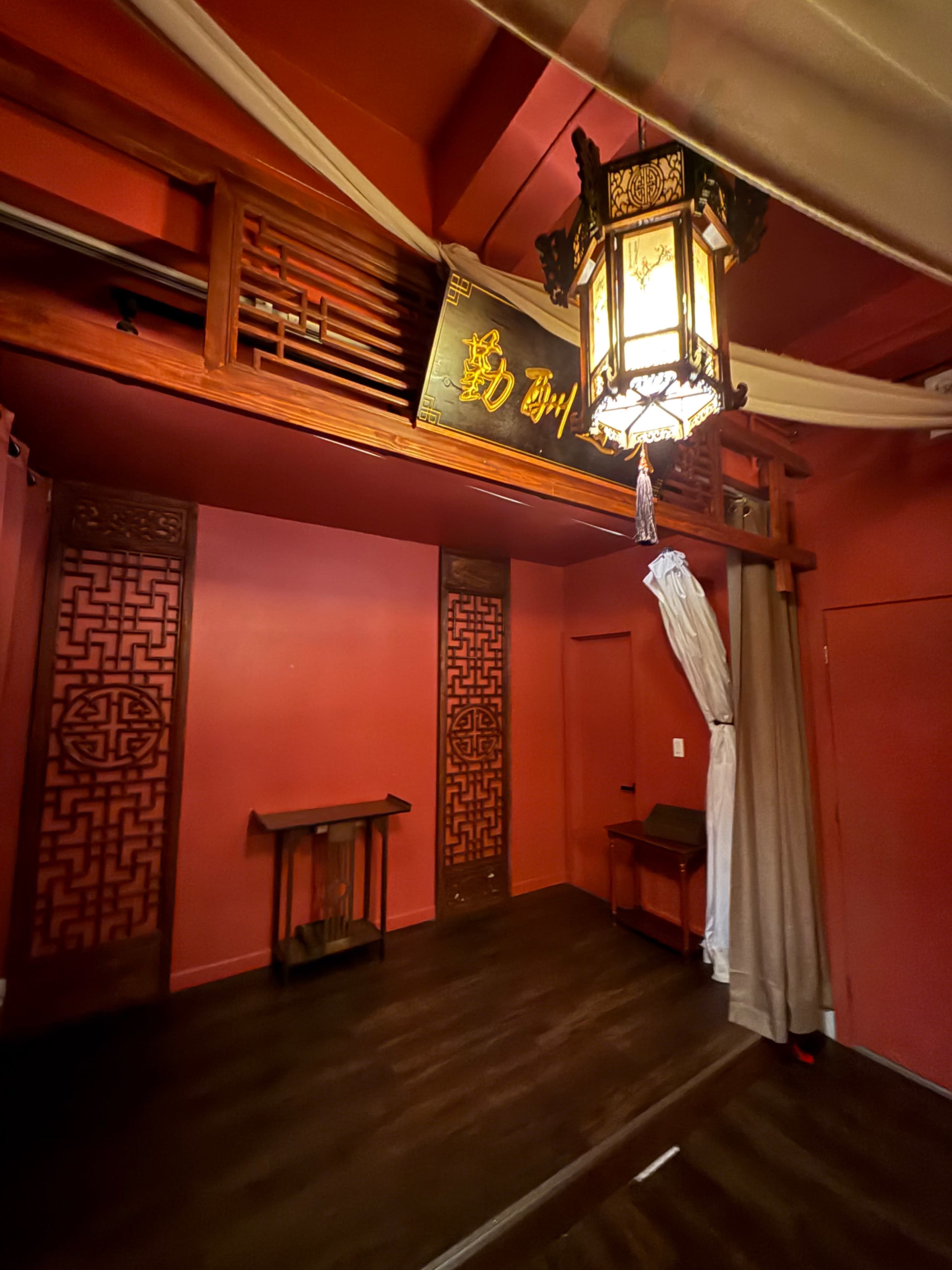 The image shows an interior space with red walls, wooden accents, and an ornate lantern hanging from the ceiling.