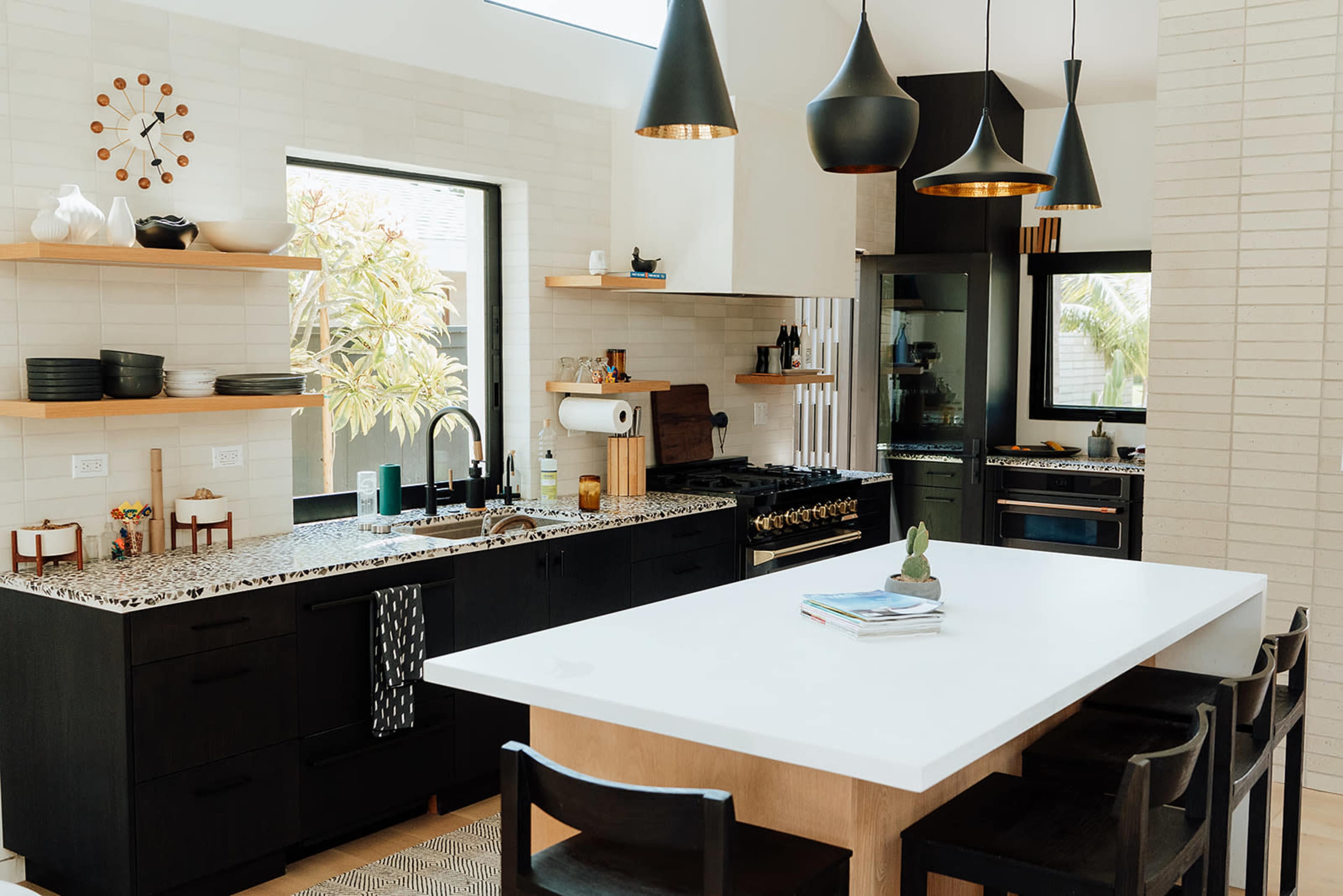 The image shows a modern kitchen with black cabinets, a large white island, and pendant lighting.