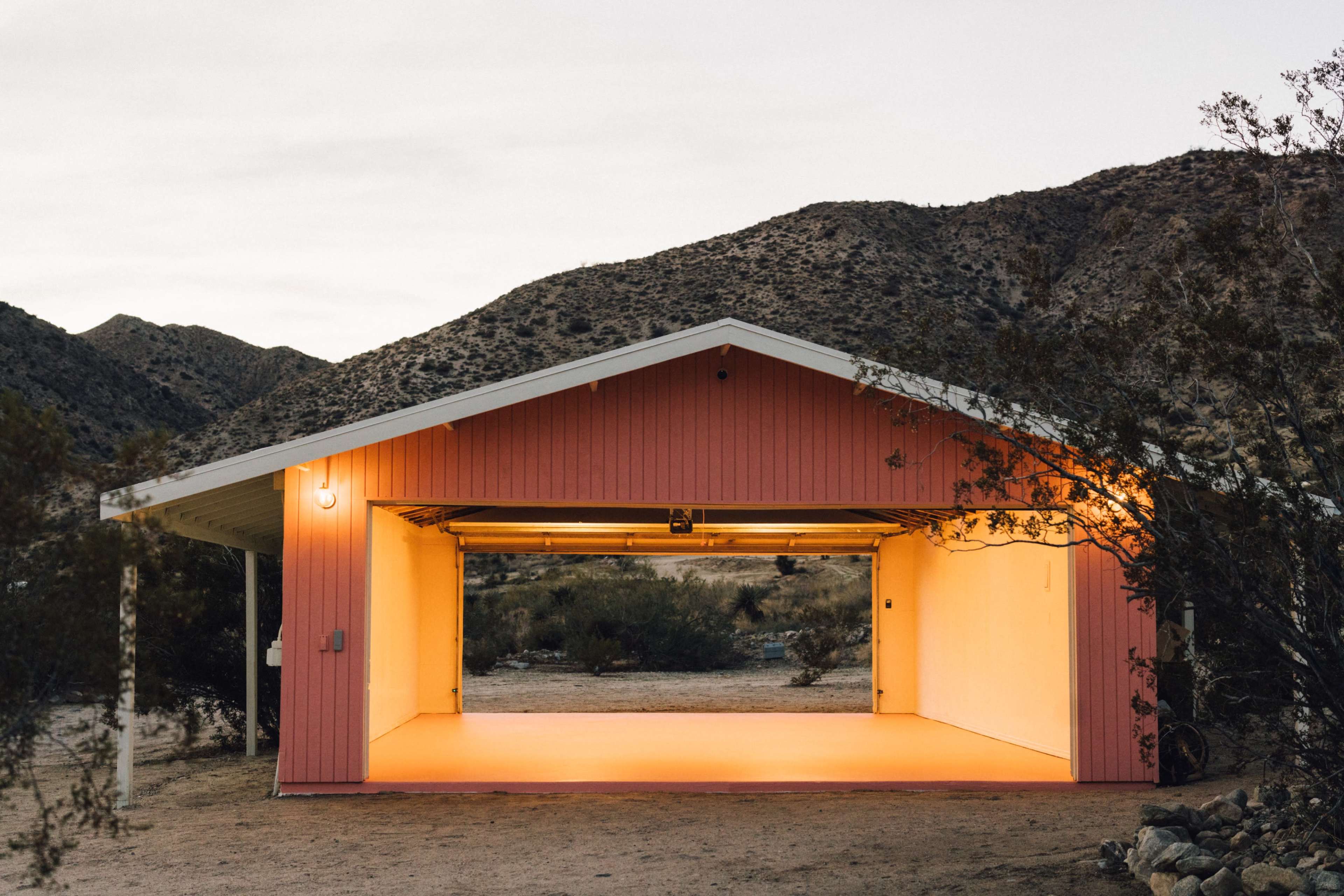 A pink garage with an open door is situated in a desert landscape surrounded by mountains.