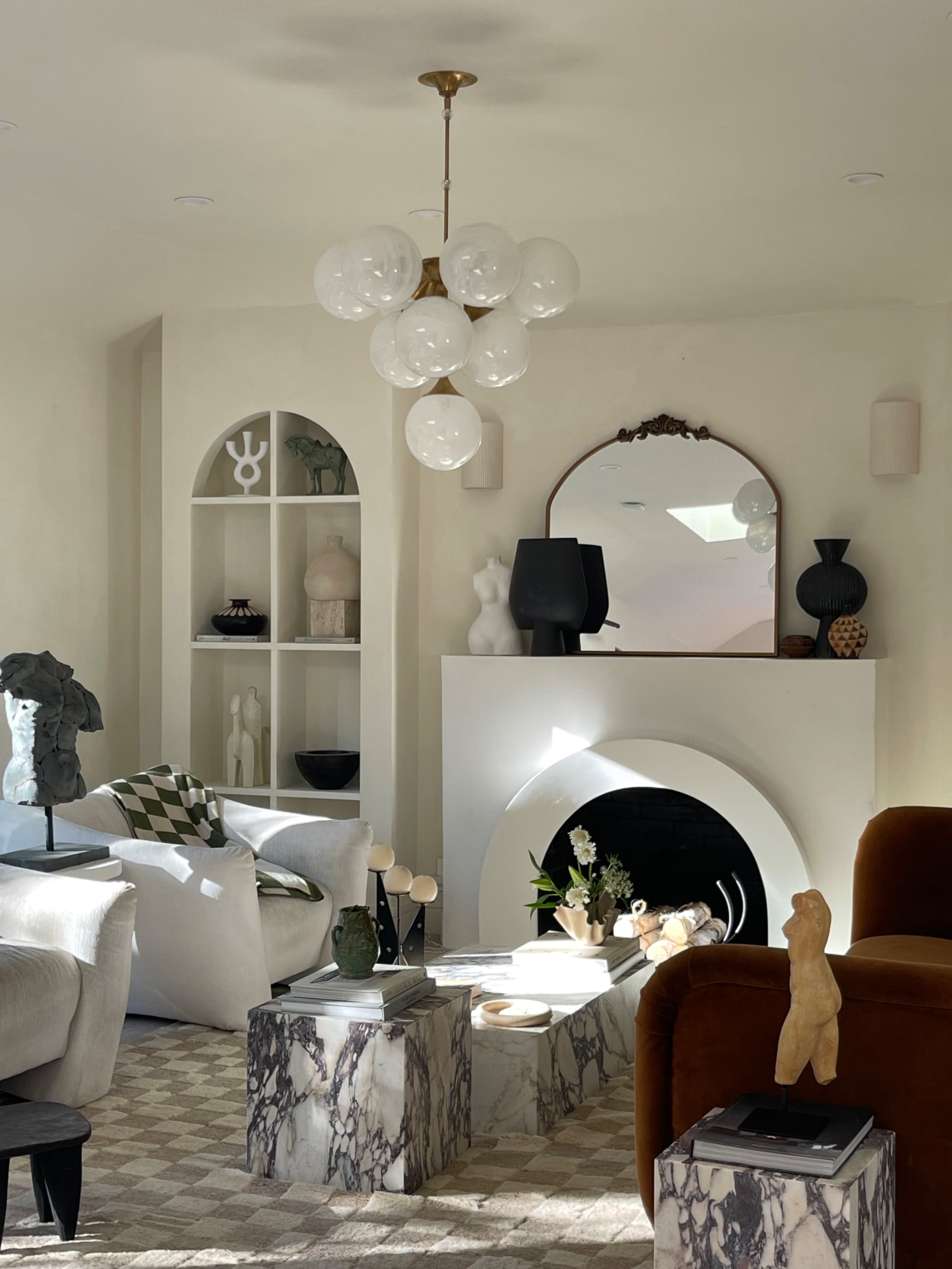 A modern living room featuring a stylish arrangement of furniture, art pieces, and decorative objects around a central fireplace.