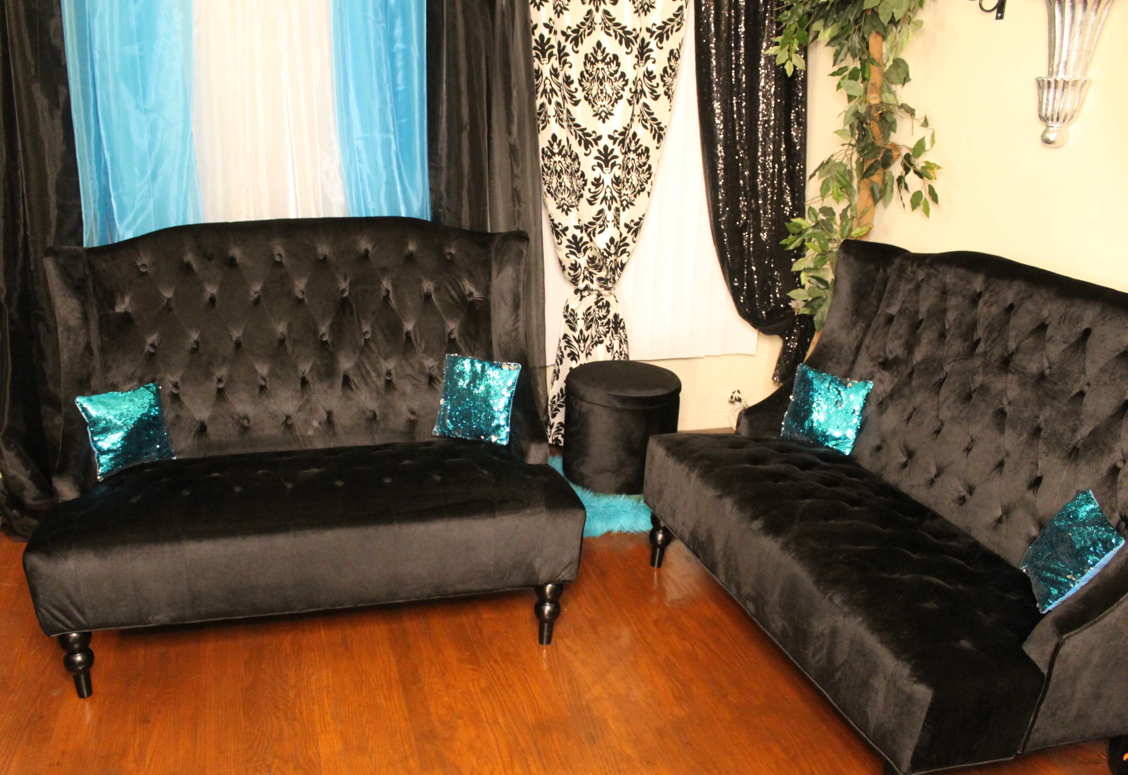 The image shows a living room with two black velvet sofas, each featuring turquoise sequin pillows, set against a backdrop of black and turquoise drapes and patterned curtains.