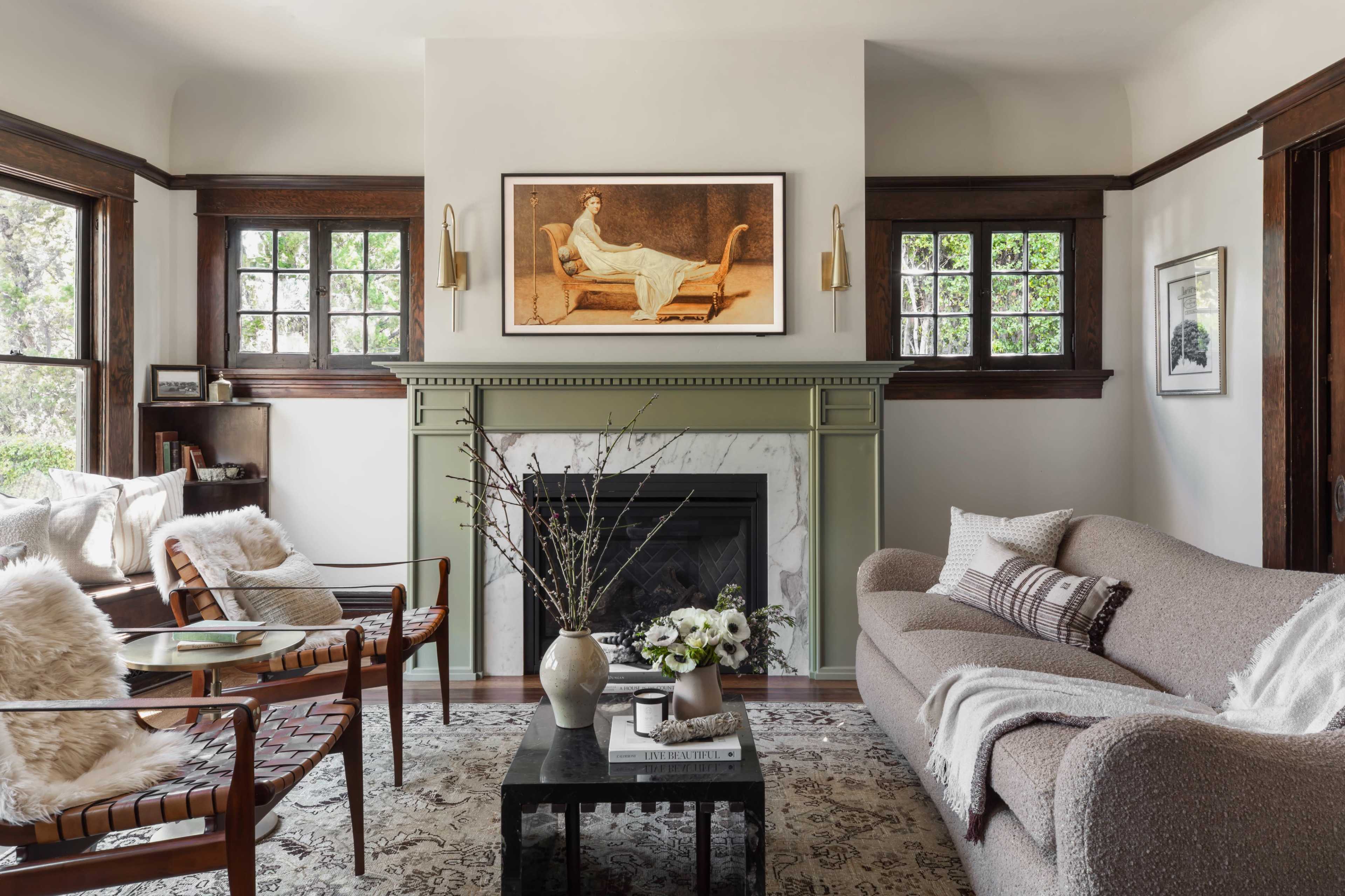 A cozy living room features a green fireplace, a beige sofa, and wooden chairs with large windows letting in natural light.