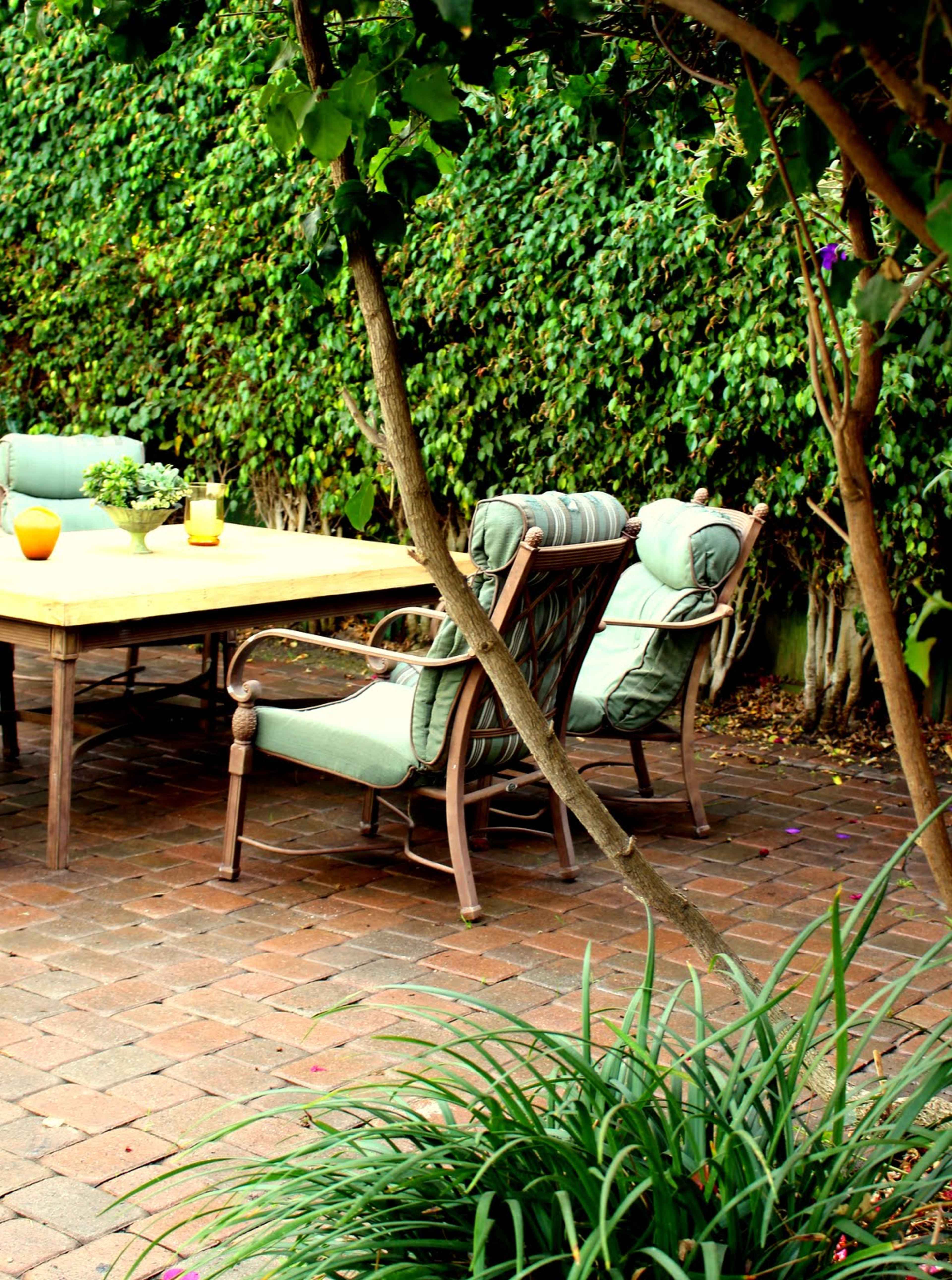 A patio setting features two chairs and a table surrounded by greenery and a paved floor.