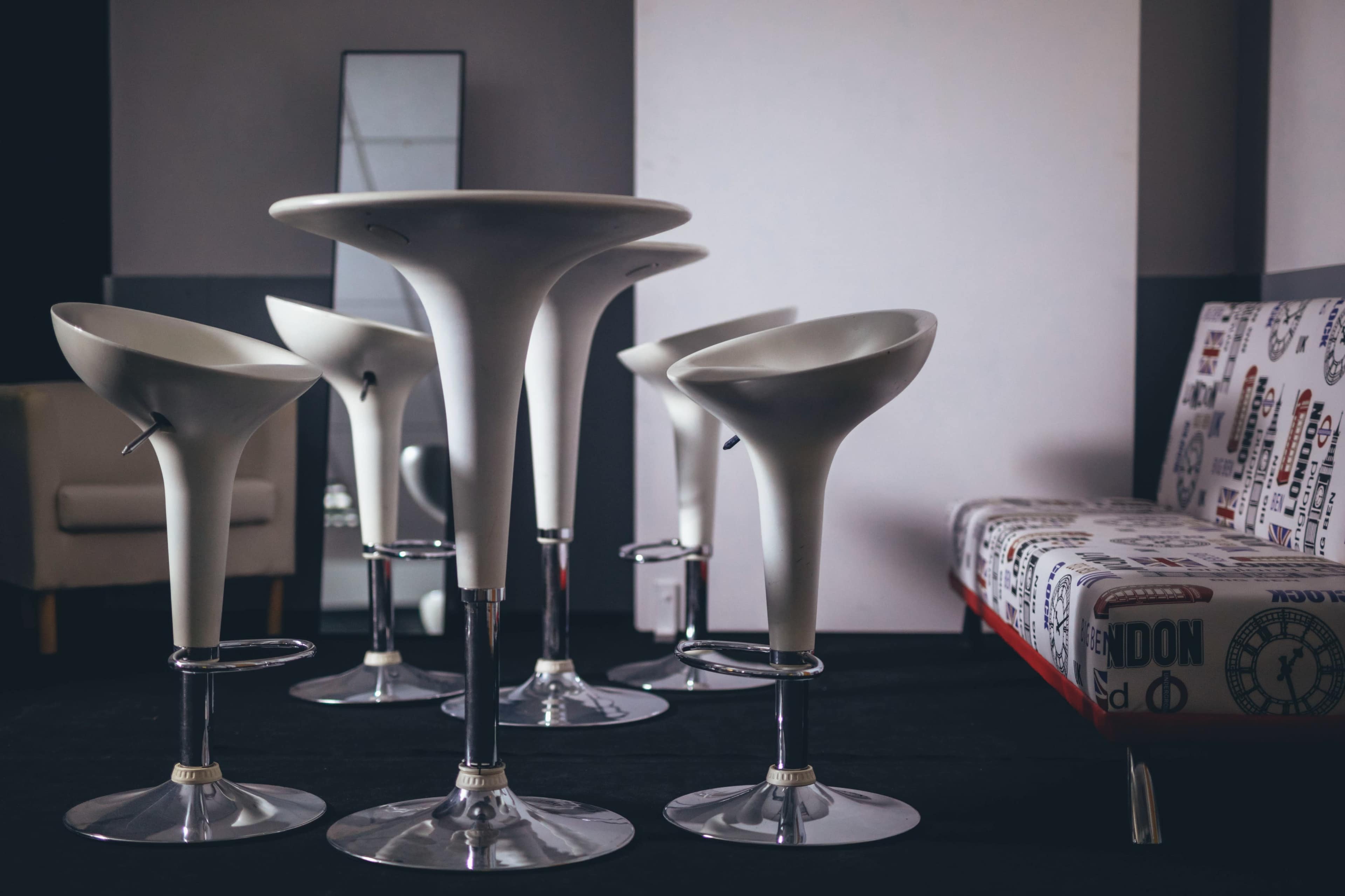 A modern seating arrangement with white bar stools and tables in a minimalist room.