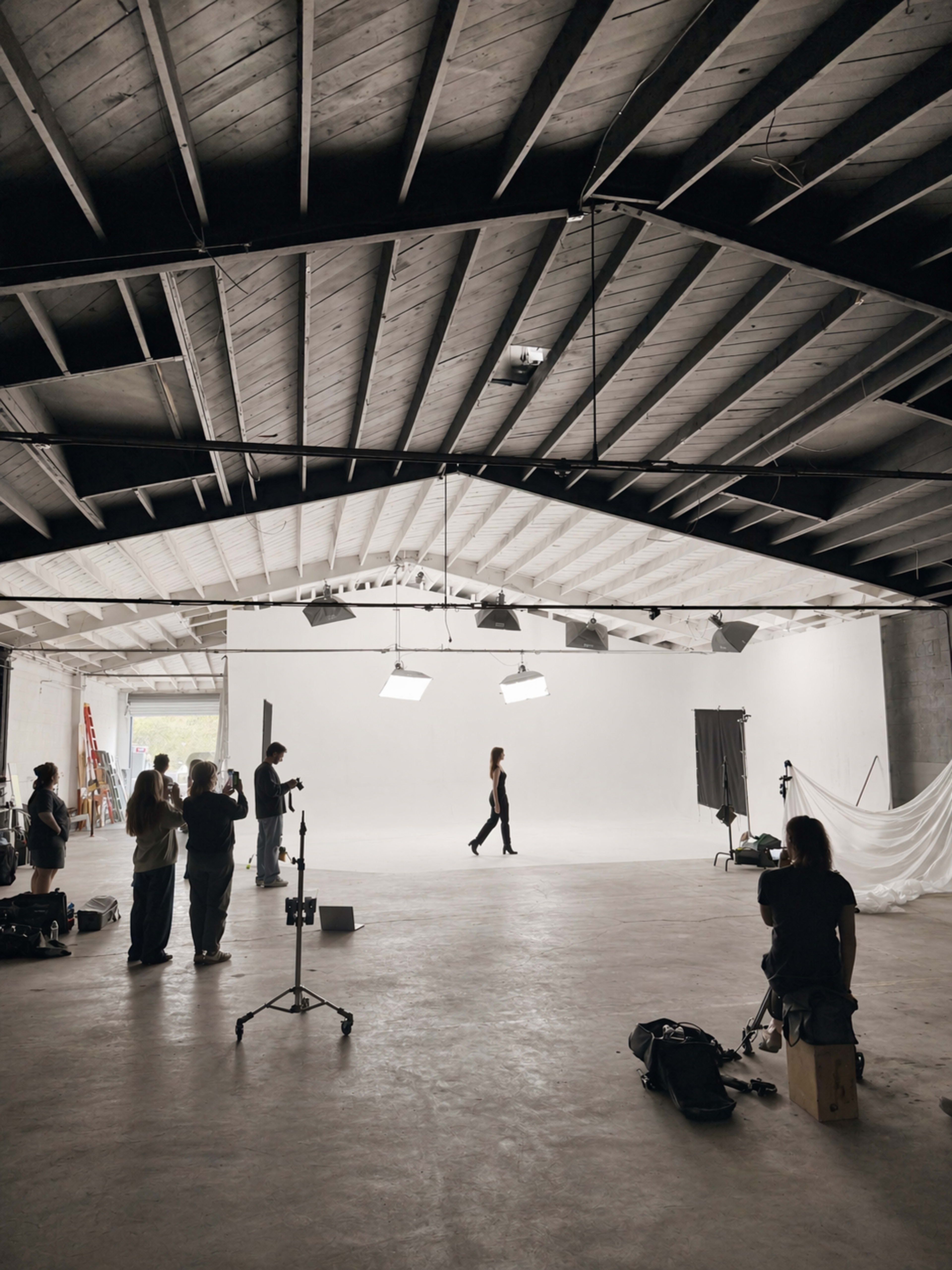 A model walks across a spacious photo studio while a crew sets up equipment and monitors the shoot.