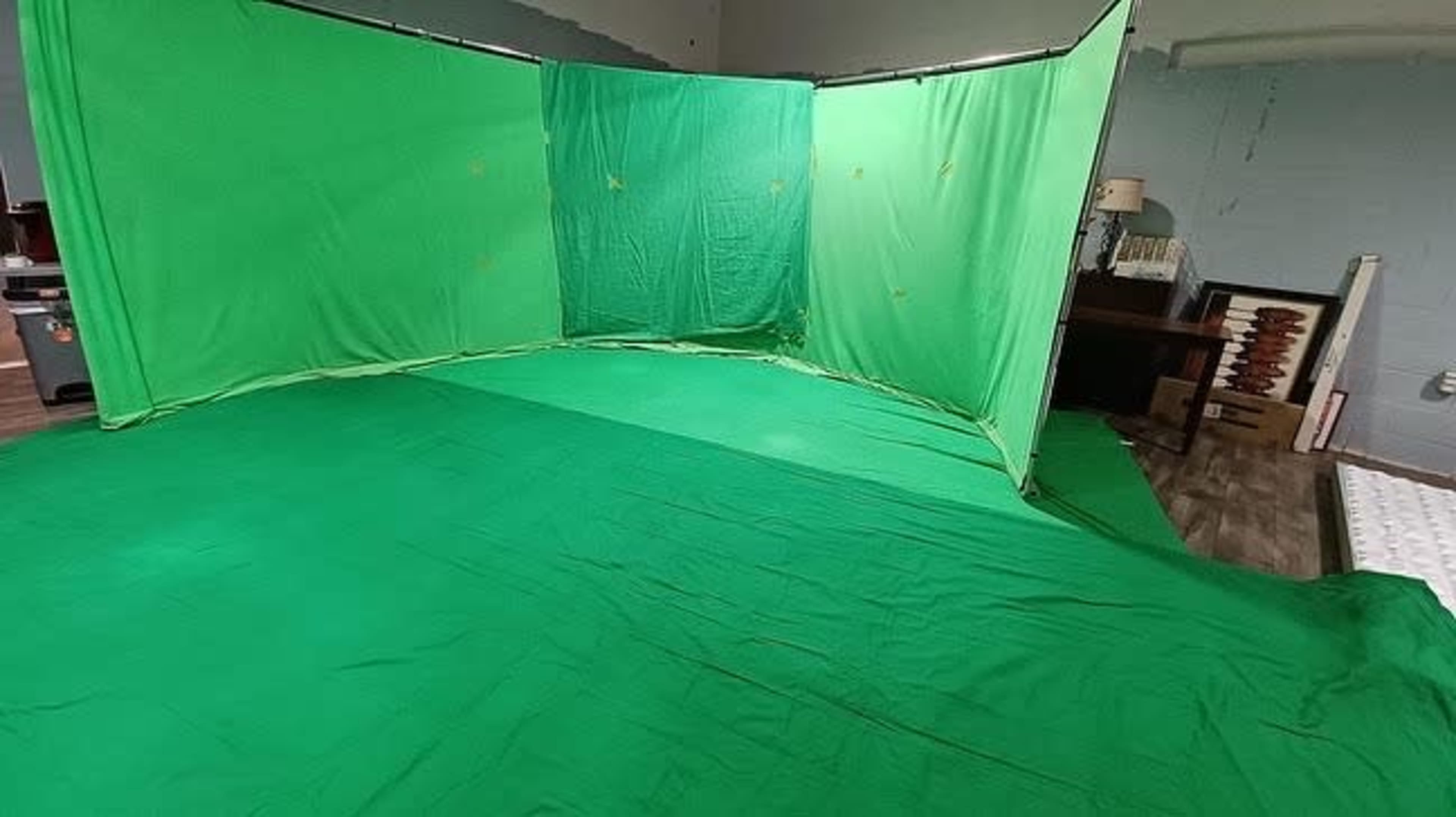 A room is set up with green fabric panels and a green floor covering, creating a green screen area for filming or photography.