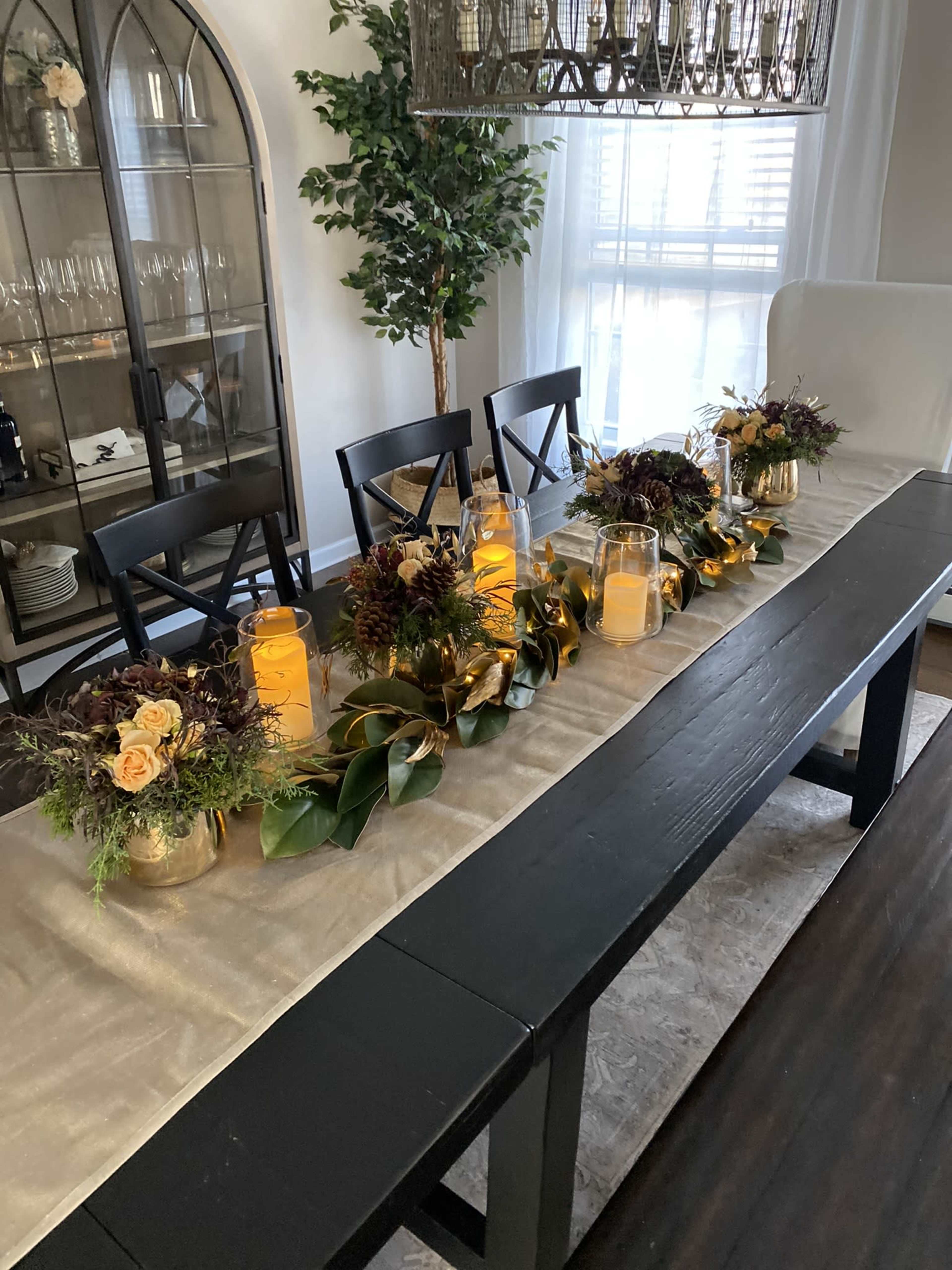 A long dining table is set with floral arrangements and jars of orange drink, surrounded by black chairs.