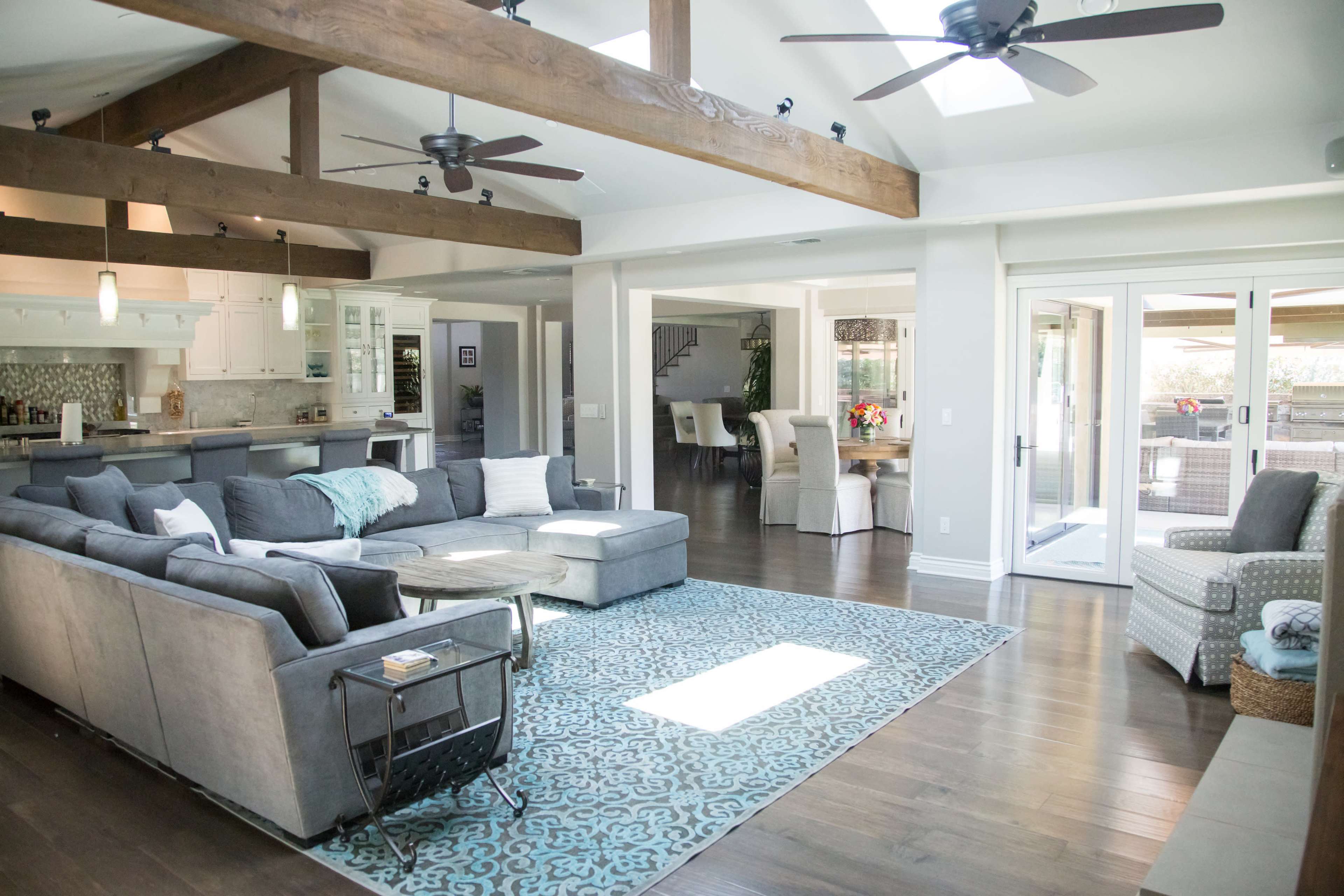 A spacious living room featuring a large sectional sofa, wooden beams on the ceiling, and sliding glass doors leading to an outdoor area.
