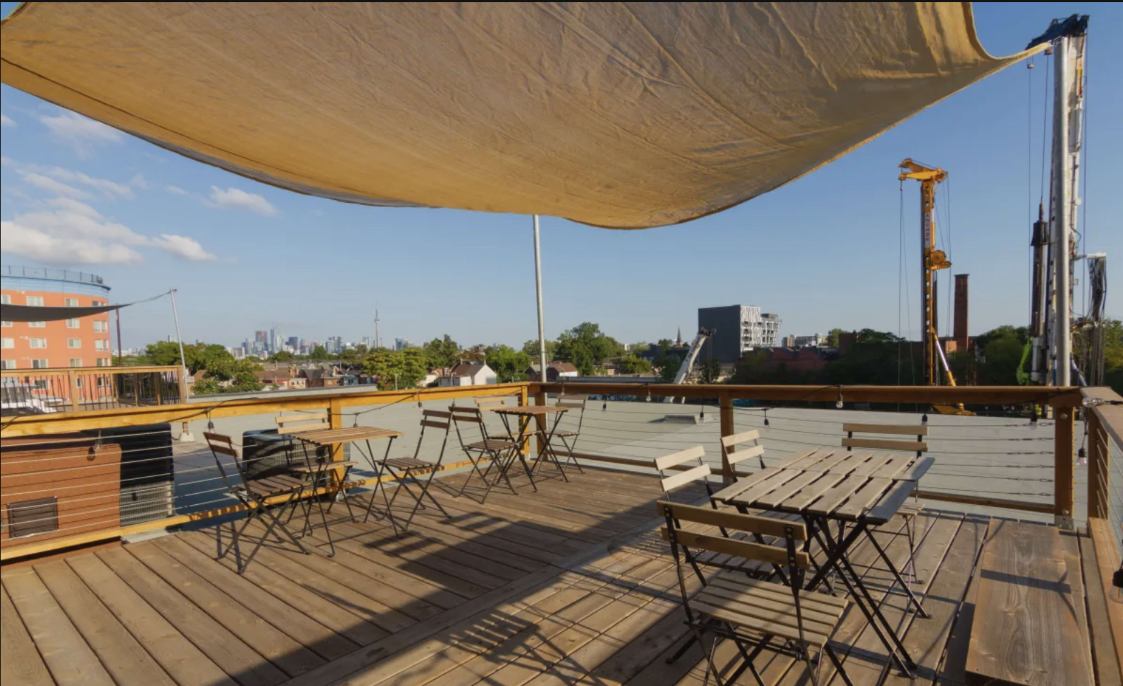 A rooftop terrace features wooden tables and chairs under a large canopy, with a city skyline visible in the background.
