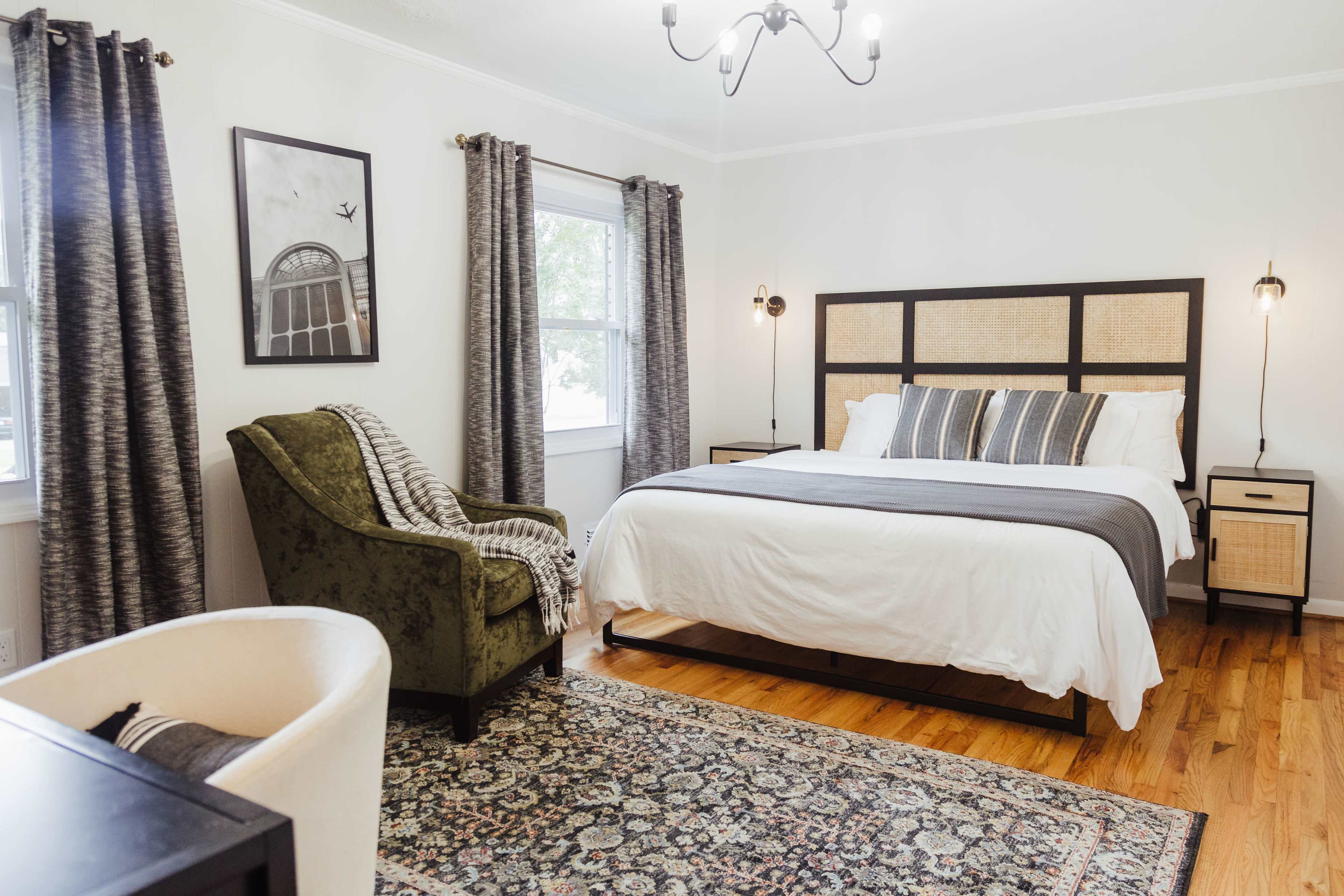 A well-decorated bedroom with a large bed, a green armchair, patterned curtains, and a decorative rug.