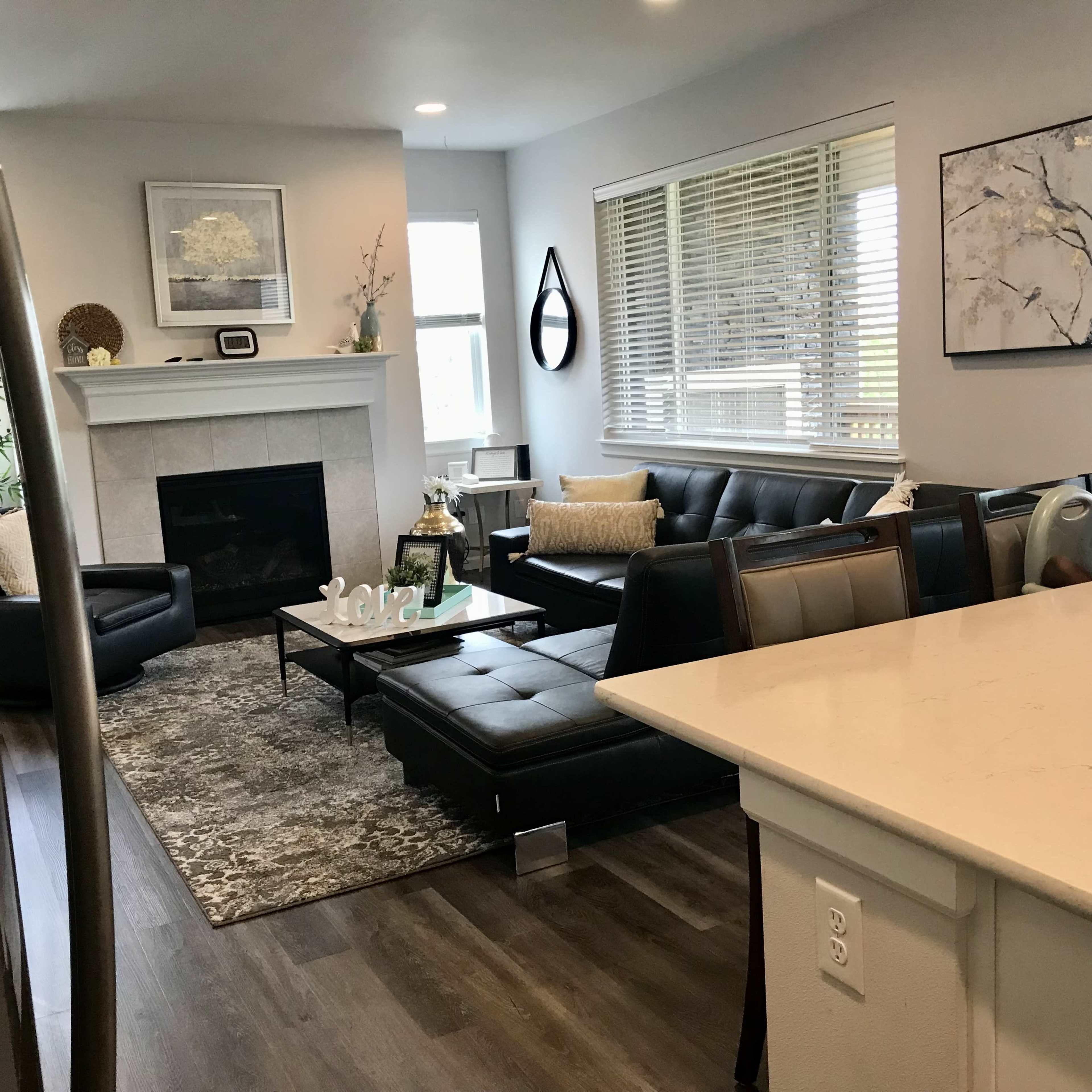 A modern living room with a fireplace, sleek black leather furniture, a coffee table, and decorative elements against light-colored walls.