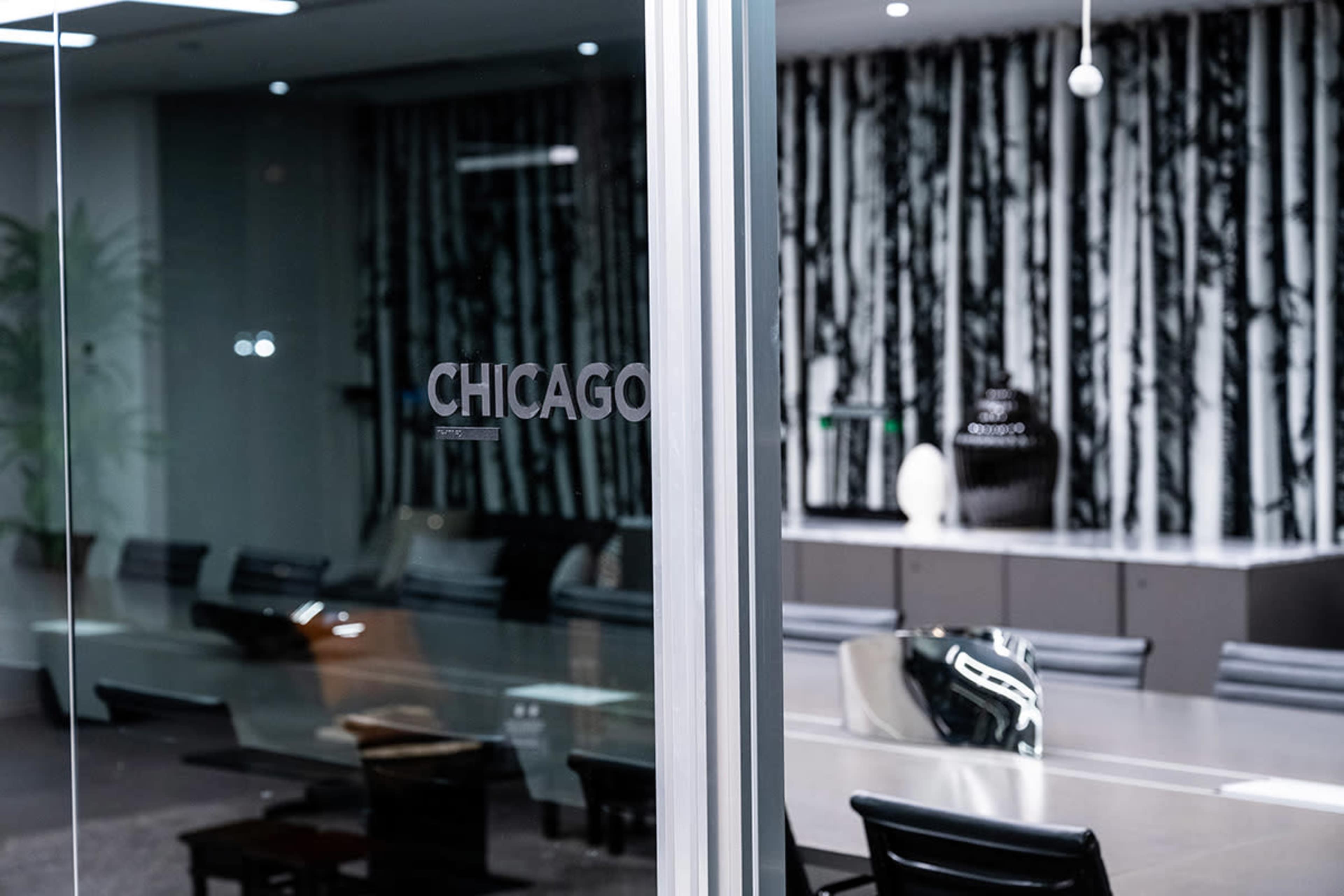 A glass door with the word "CHICAGO" etched on it leads into a modern conference room featuring a large table and a backdrop of black and white patterned wallpaper.