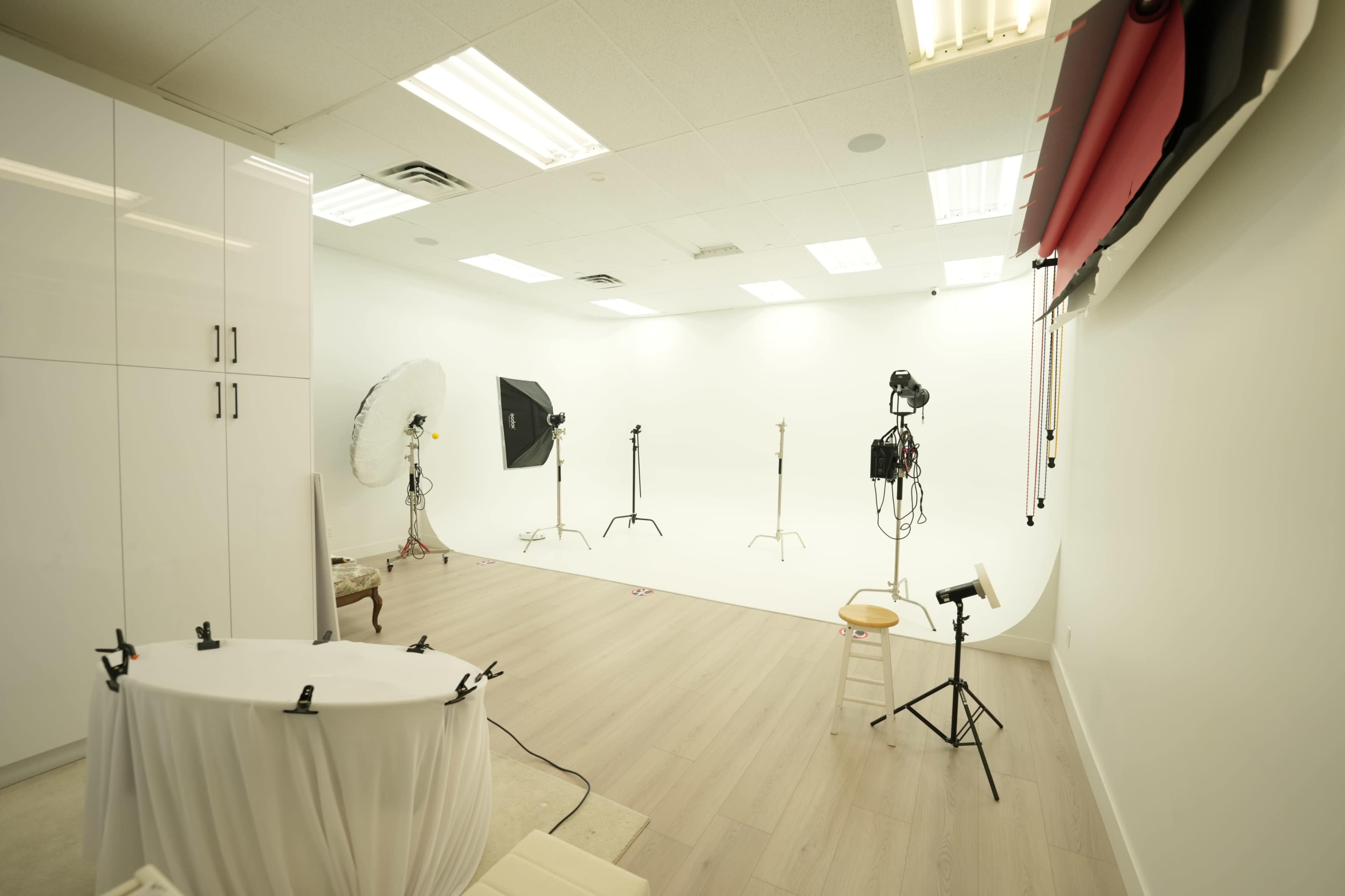 The image shows a photo studio featuring a white backdrop, lighting equipment, and various props arranged in an organized manner.