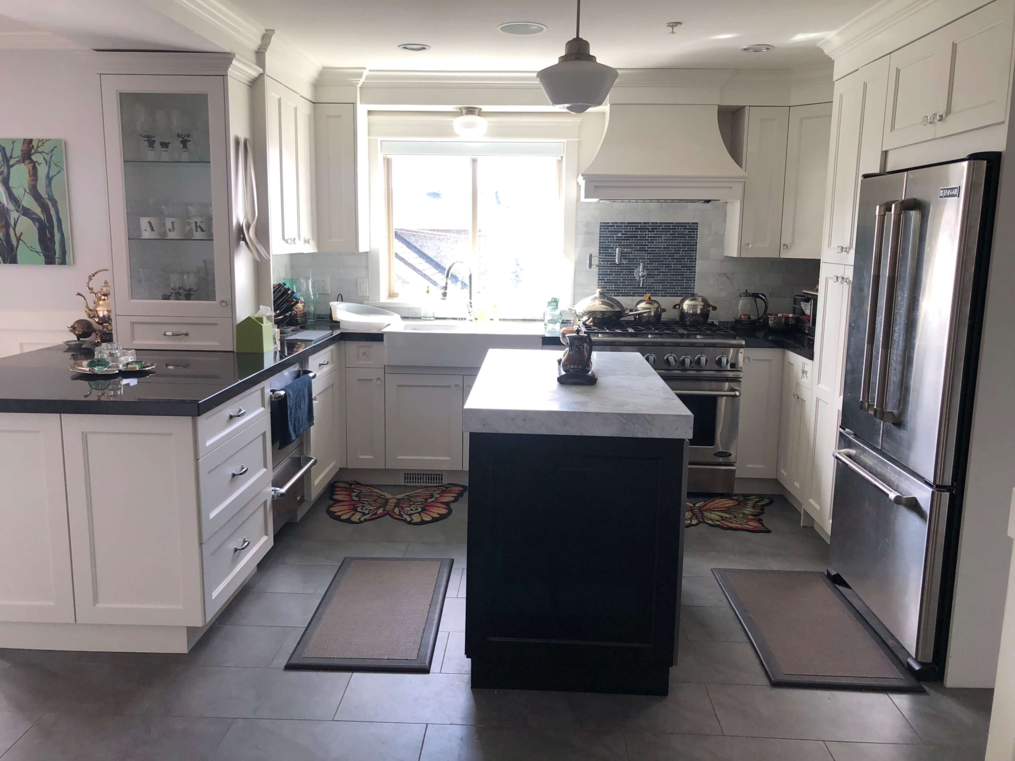 A modern kitchen with white cabinetry, a central island, and stainless steel appliances, illuminated by natural light from a window.