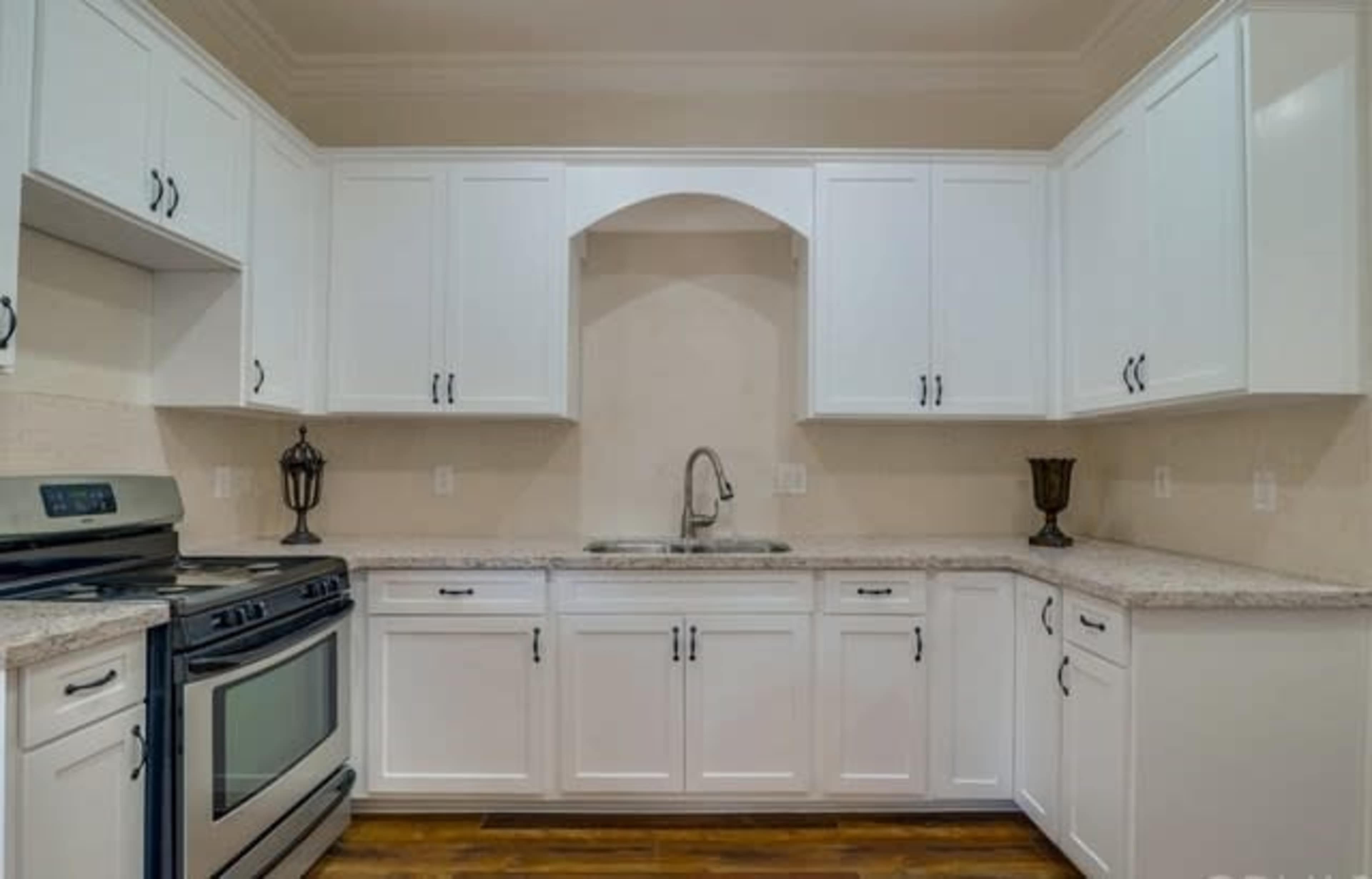 The image shows a modern kitchen with white cabinets, a stainless steel stove, and a granite countertop.