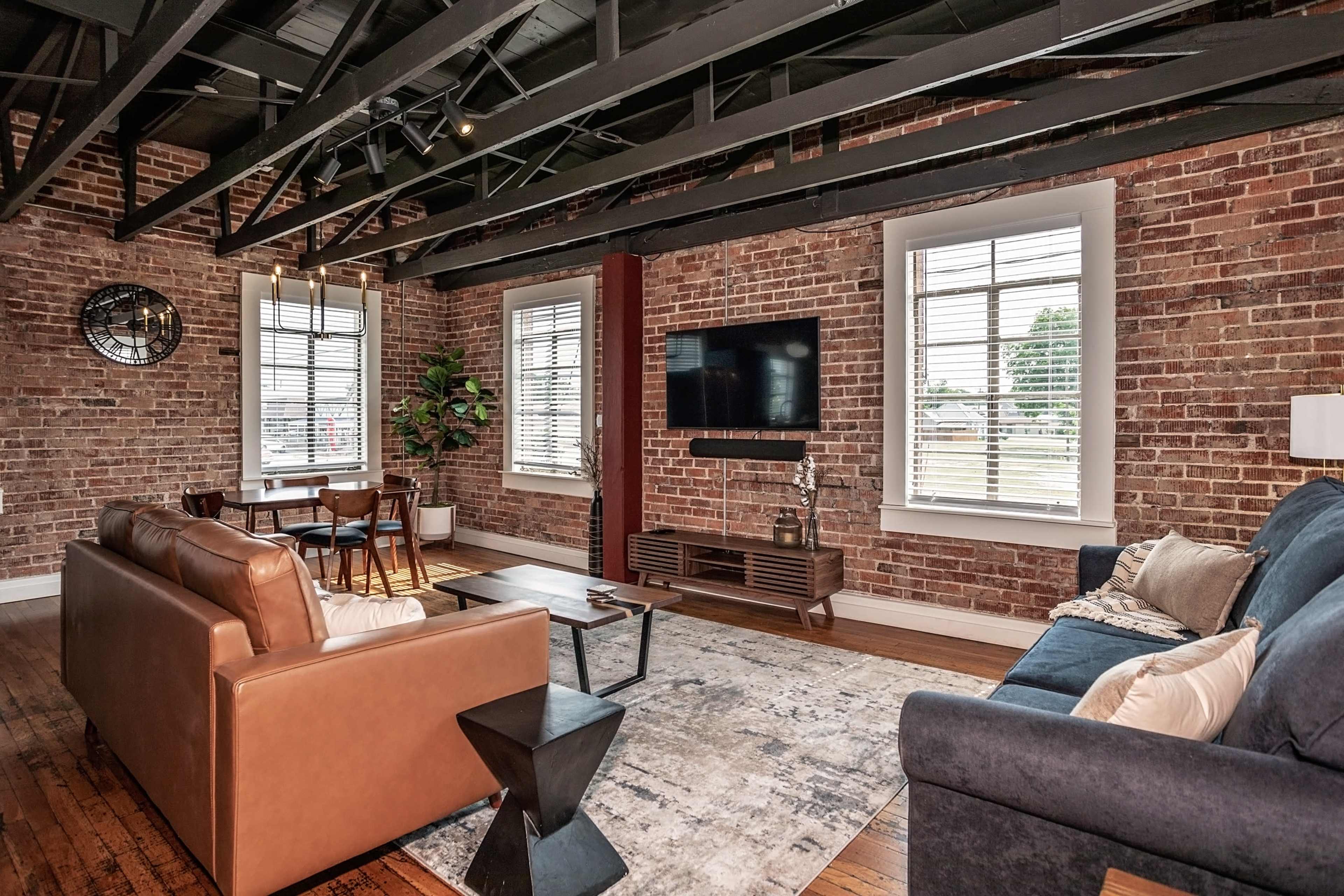 A modern living room with exposed brick walls, wooden floors, and a mix of seating and a television setup.