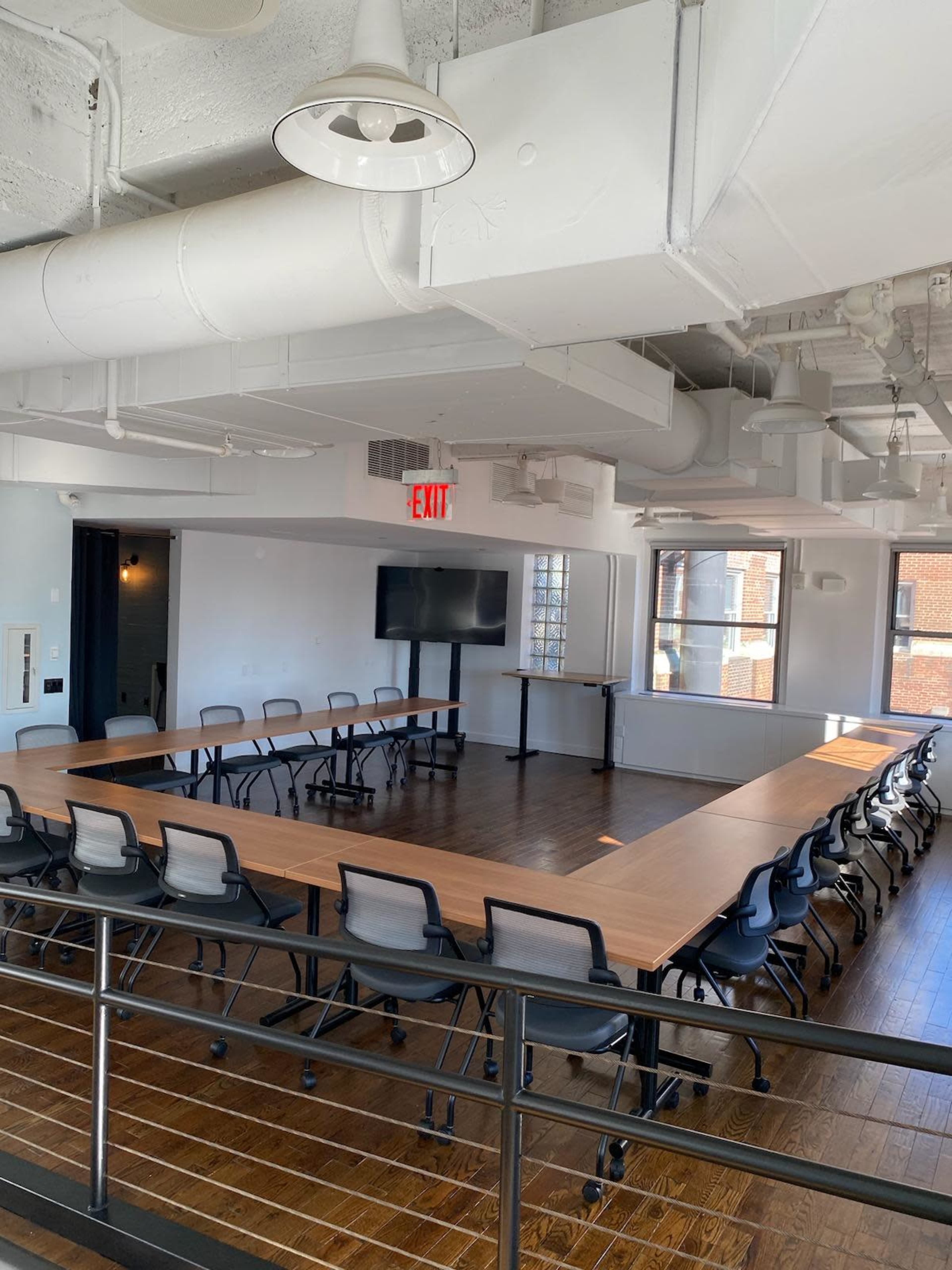 A conference room features a rectangular table surrounded by black chairs, with a large screen displayed on a stand.