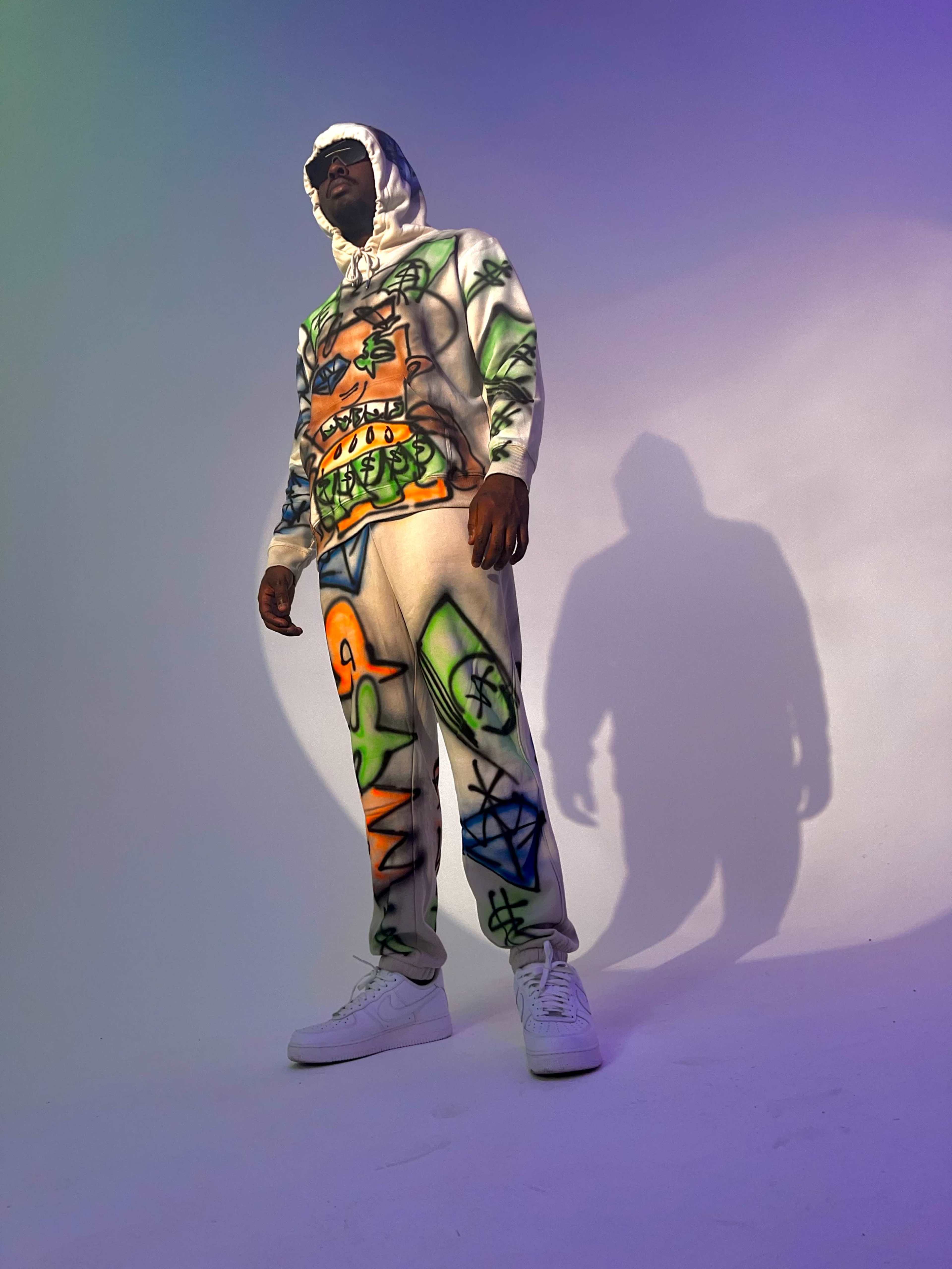 A person stands in a colorful, graffiti-patterned tracksuit against a softly lit backdrop.