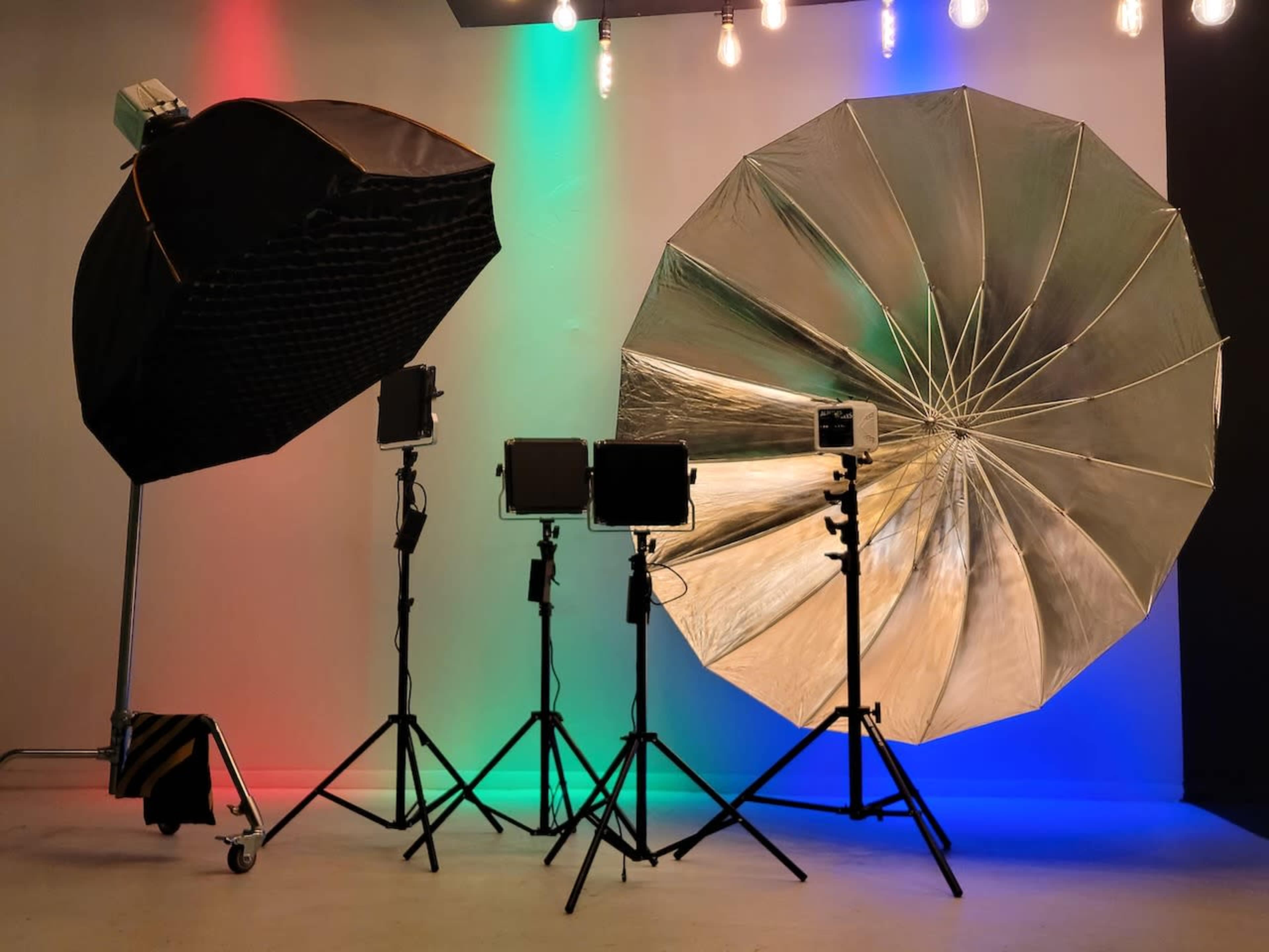 Studio lighting equipment, including softbox and umbrella lights, set up against a backdrop with colored lighting.