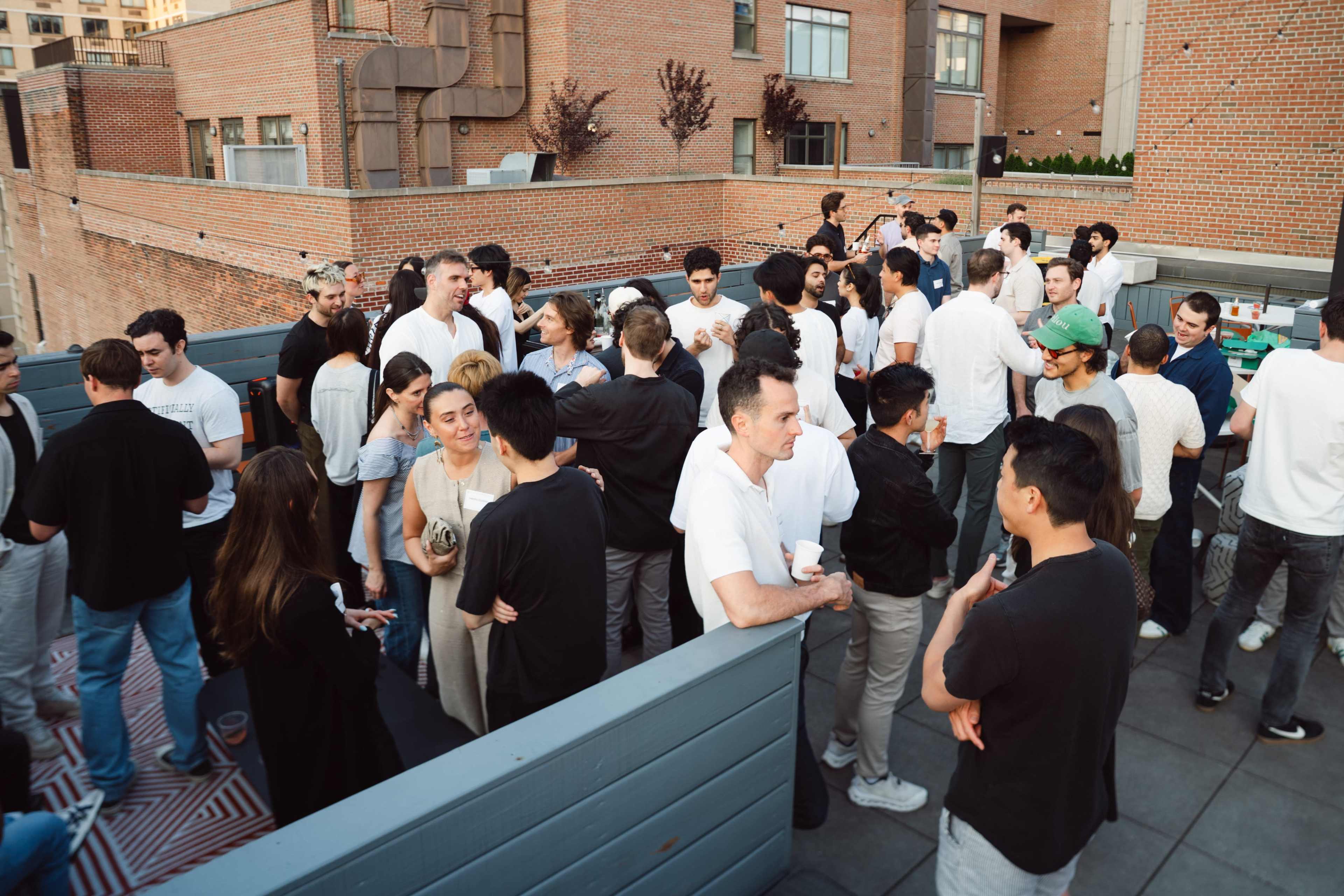 A large group of people is socializing on a rooftop terrace surrounded by brick buildings.