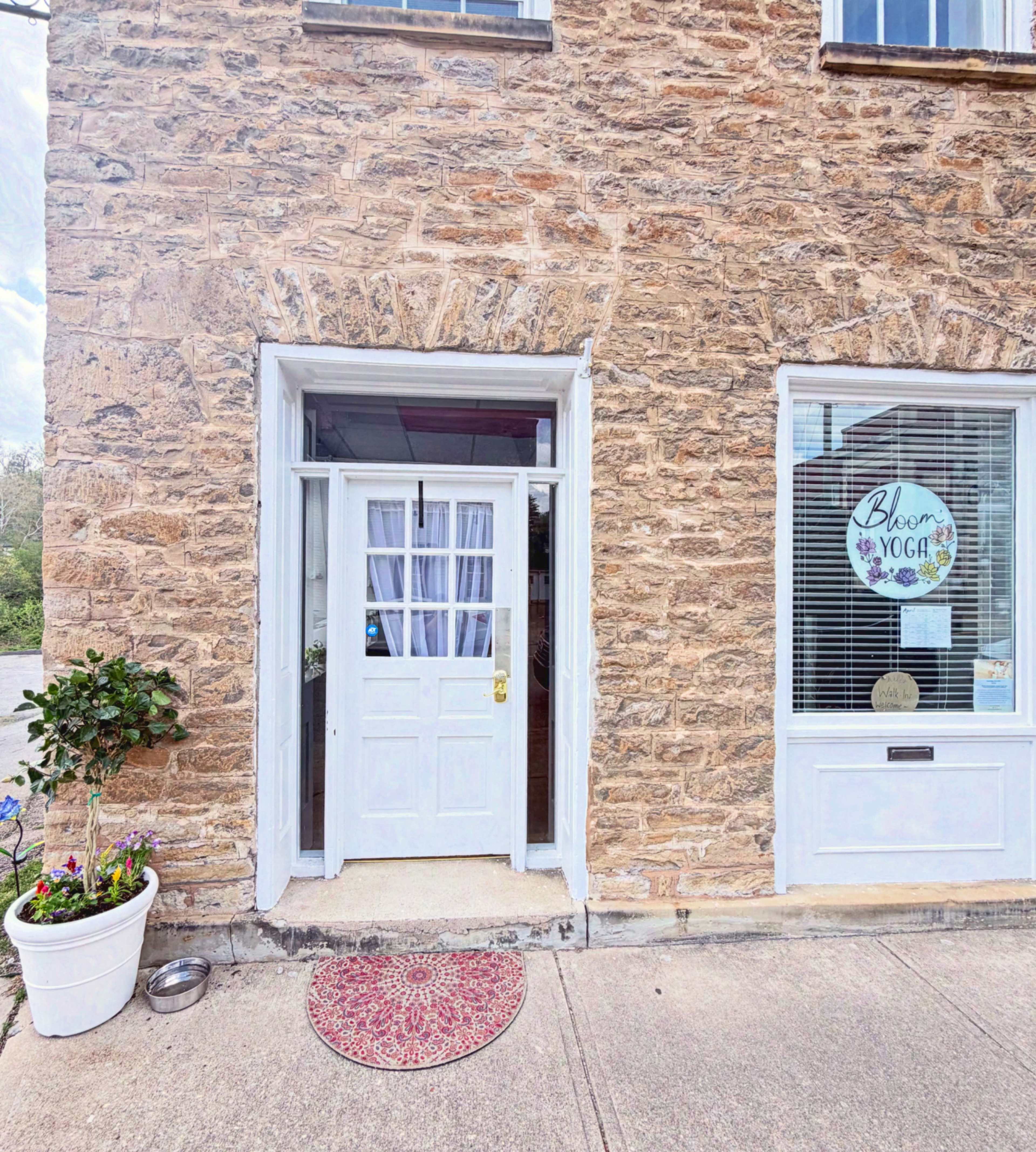 The image shows the entrance of a stone building featuring a white door with a glass panel and a yoga studio sign in the window.