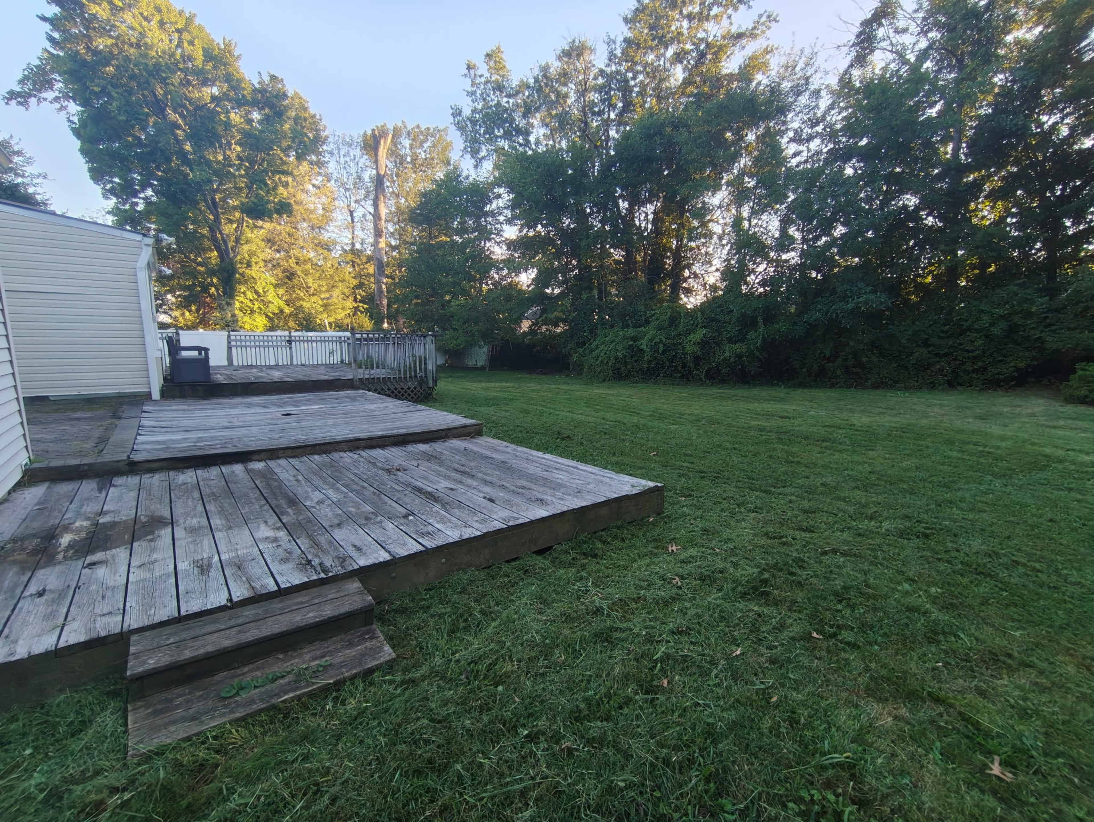 A wooden deck leads to a grassy yard surrounded by trees in the background.