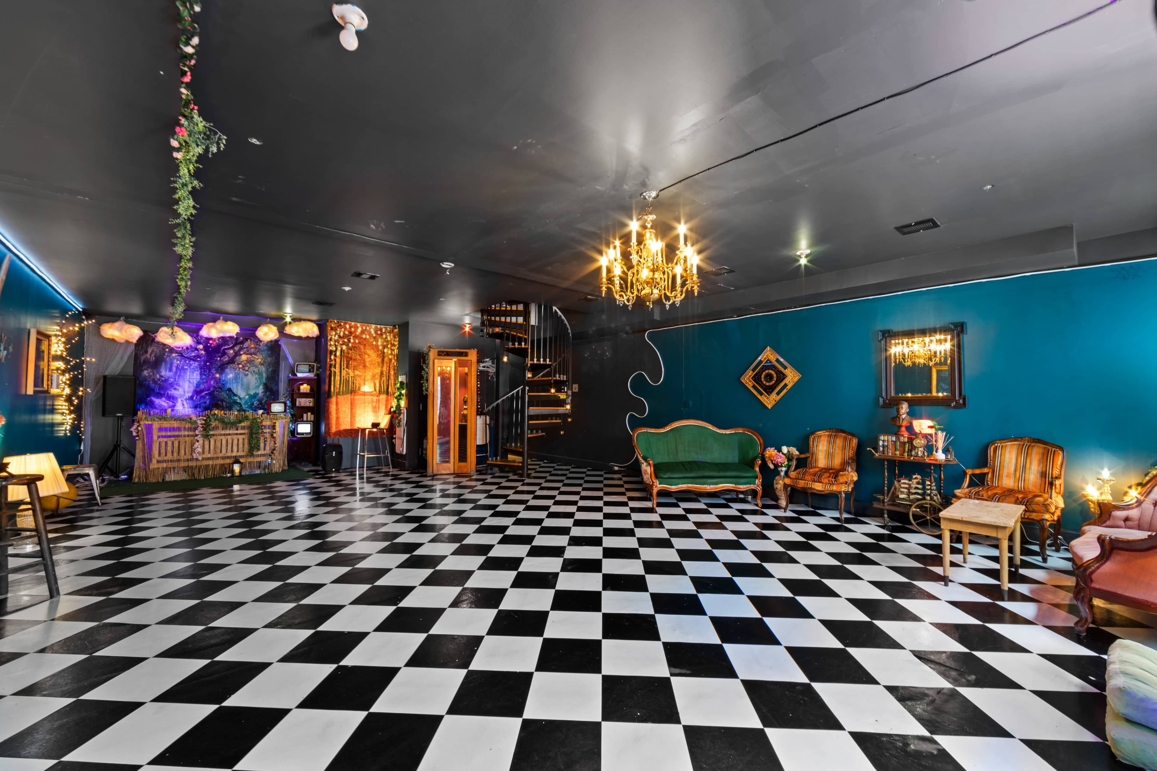 A spacious room with a checkered black and white floor, teal walls, and decorative lighting, including a chandelier and wall-mounted mirrors.