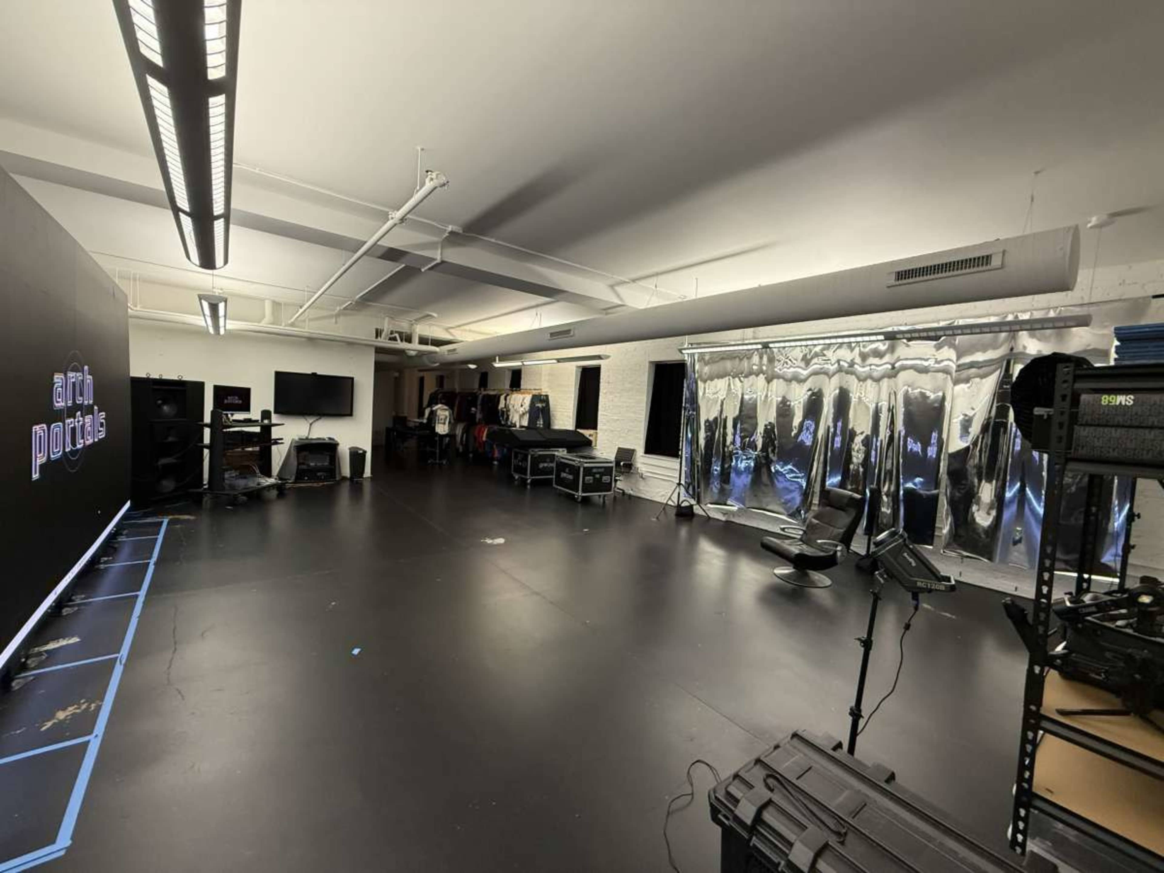The image shows a spacious studio with dark flooring, various equipment, and a wall featuring the word "art" in blue.