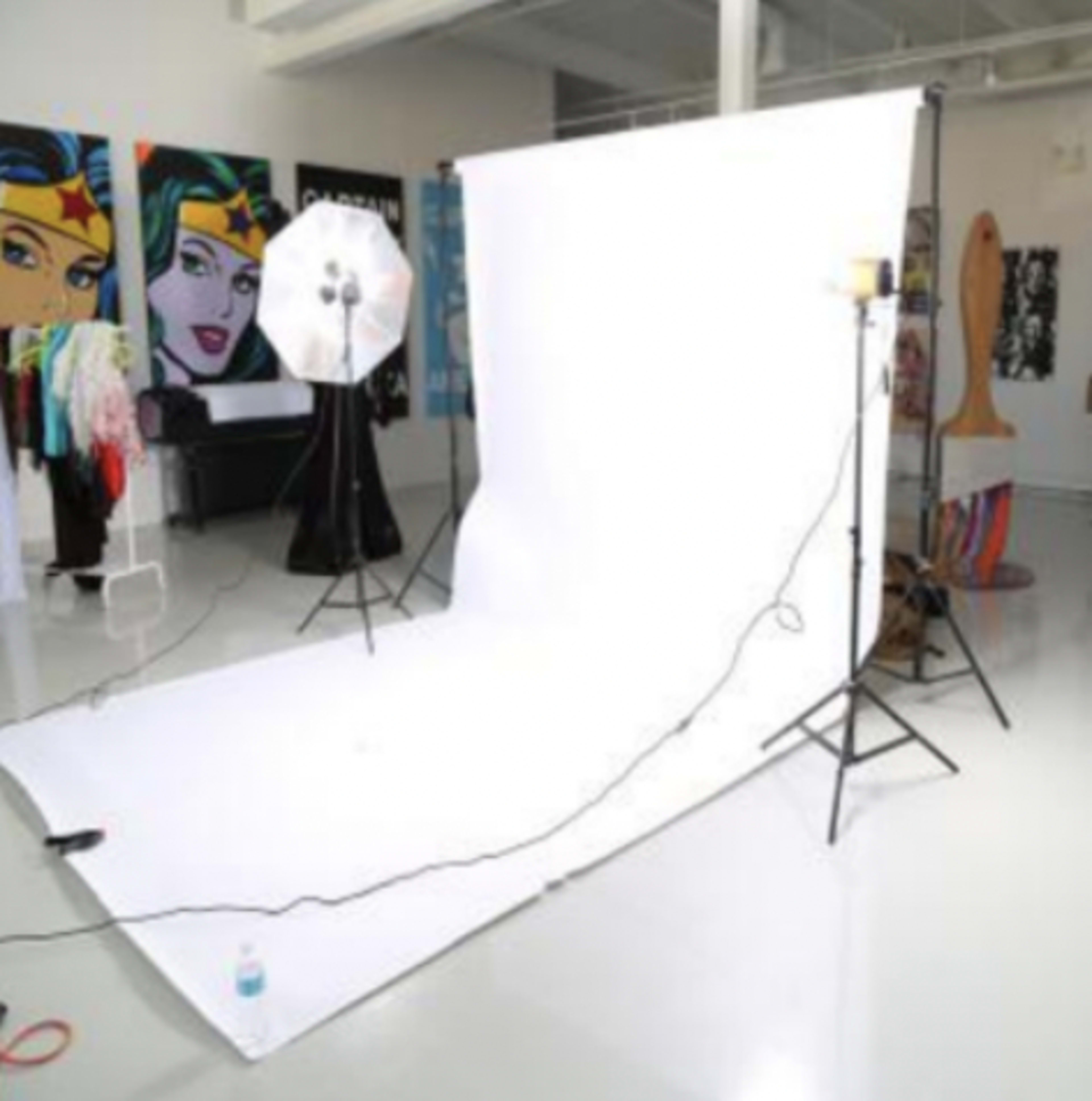 A photography studio setup with a white backdrop, studio lights, and various clothing items in the background.