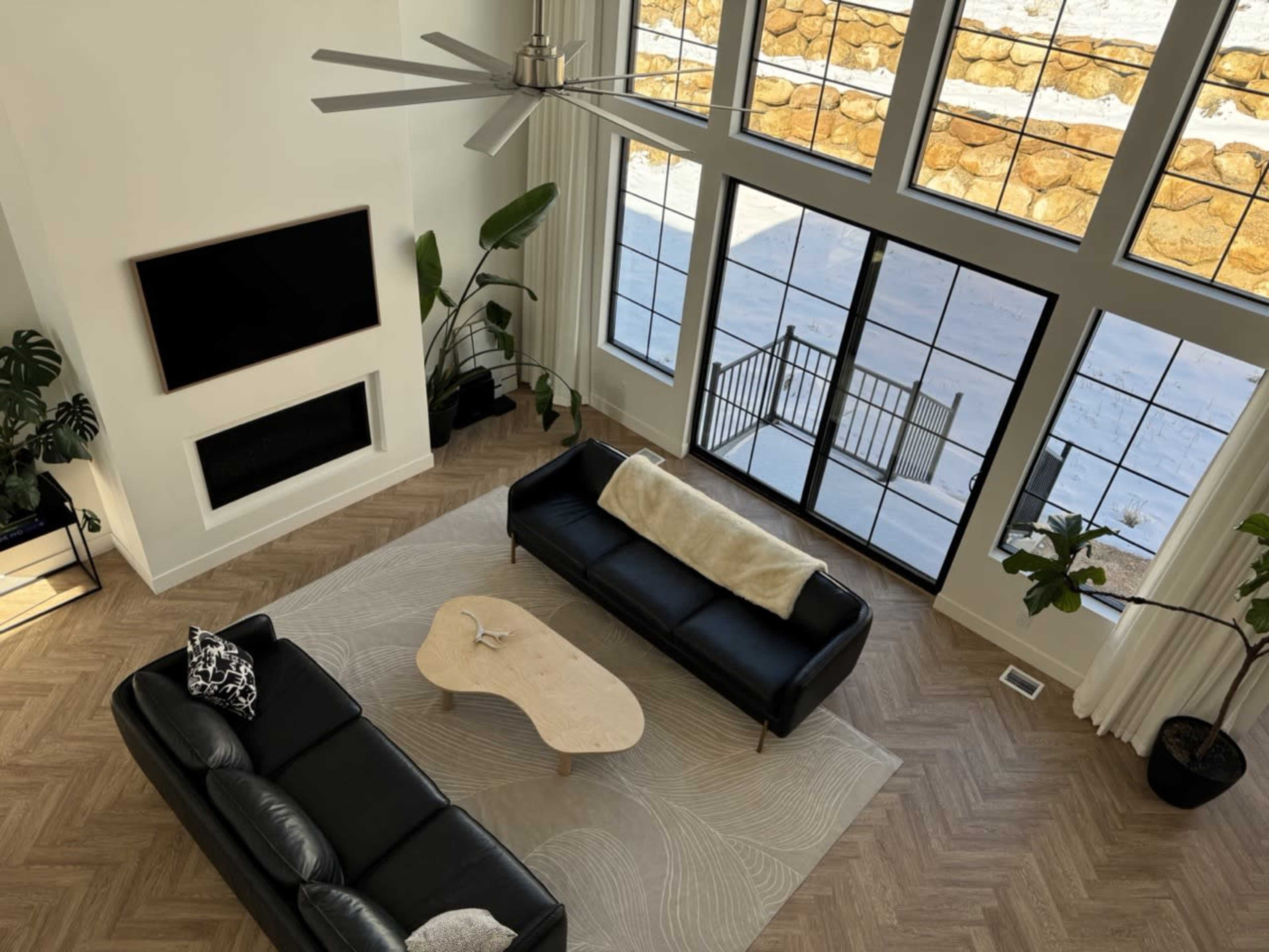 A spacious living room features two black sofas facing a large window with a view of a snowy landscape.