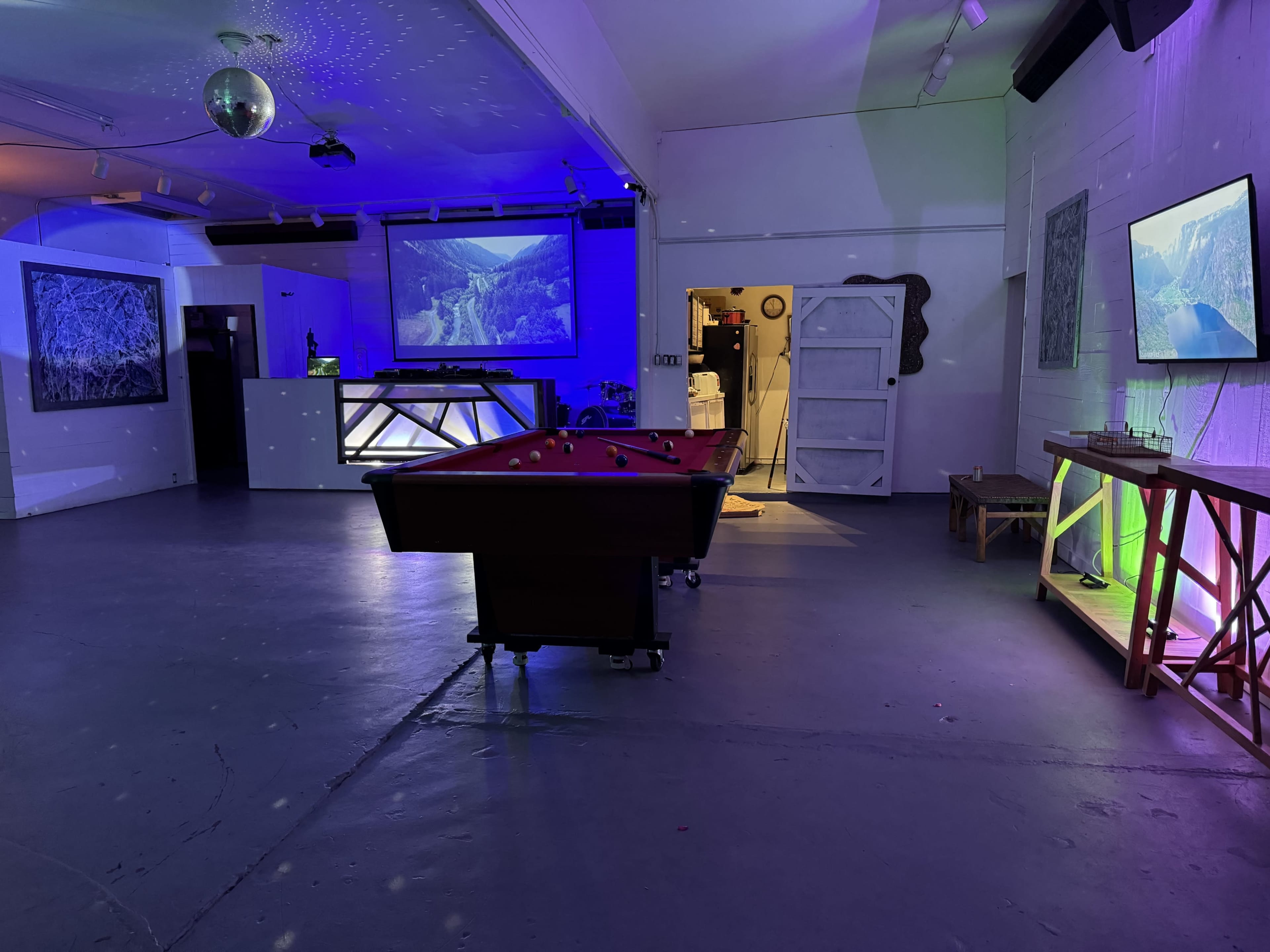 The image shows a dimly lit room with a pool table, a bar area, and multiple screens displaying landscapes.