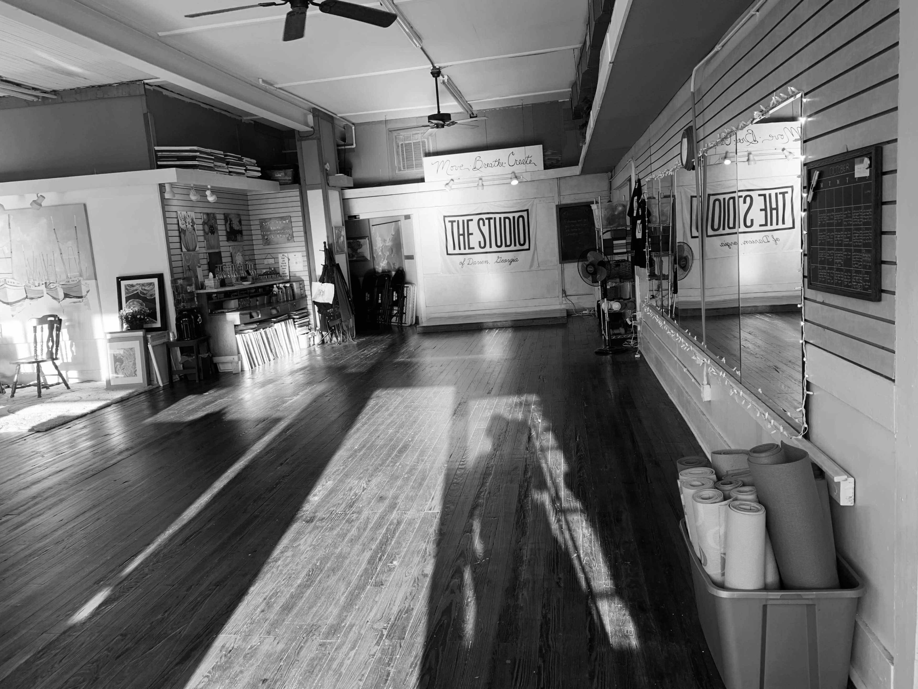 The image shows an empty dance studio with wooden floors, large mirrors, and a wall displaying the sign "THE STUDIO."